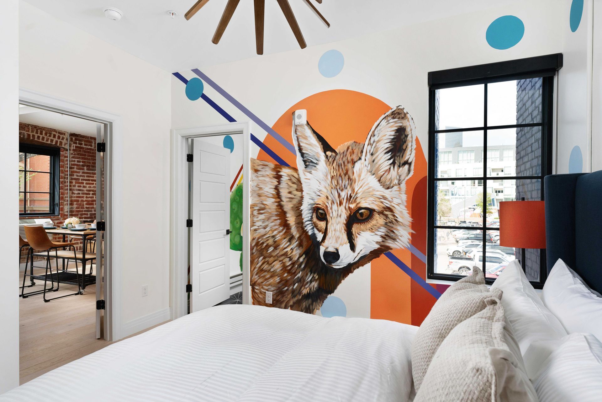 Bedroom with fox wall mural, white bedding, and a black-framed window overlooking a colorful accent wall
