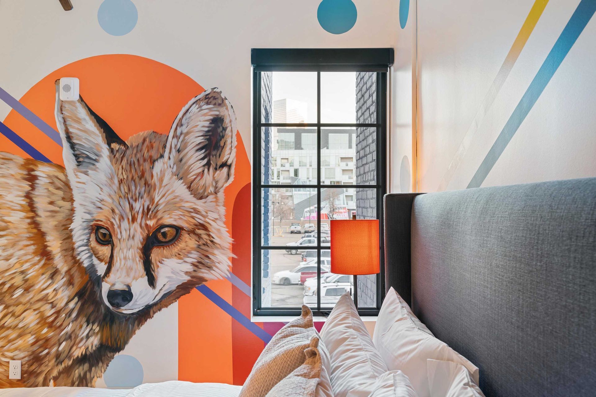 Fox mural in a colorful bedroom with a gray bed, black window, and orange lamp