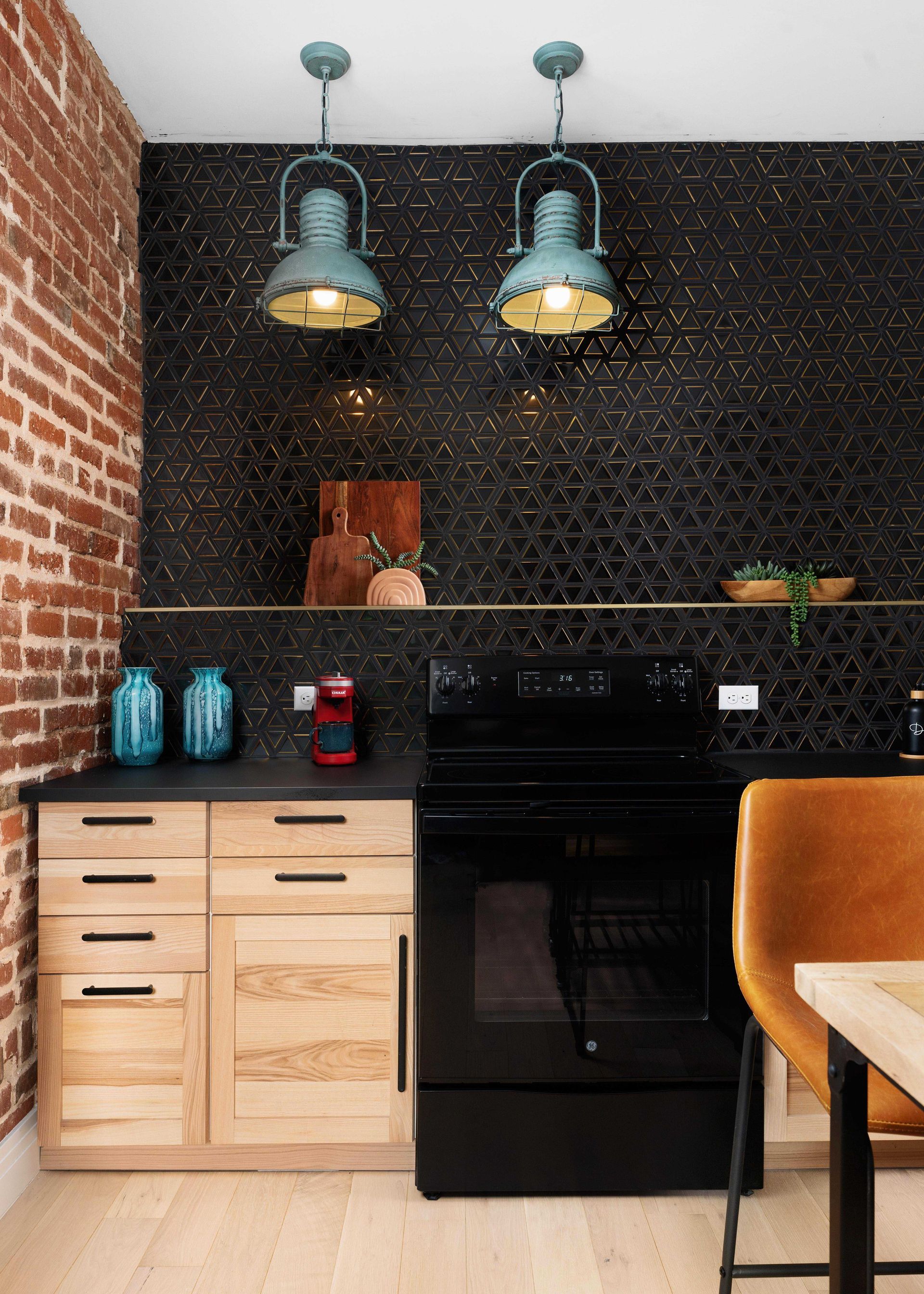 Compact kitchen with black backsplash, wooden cabinets, pendant lights, and black stove.