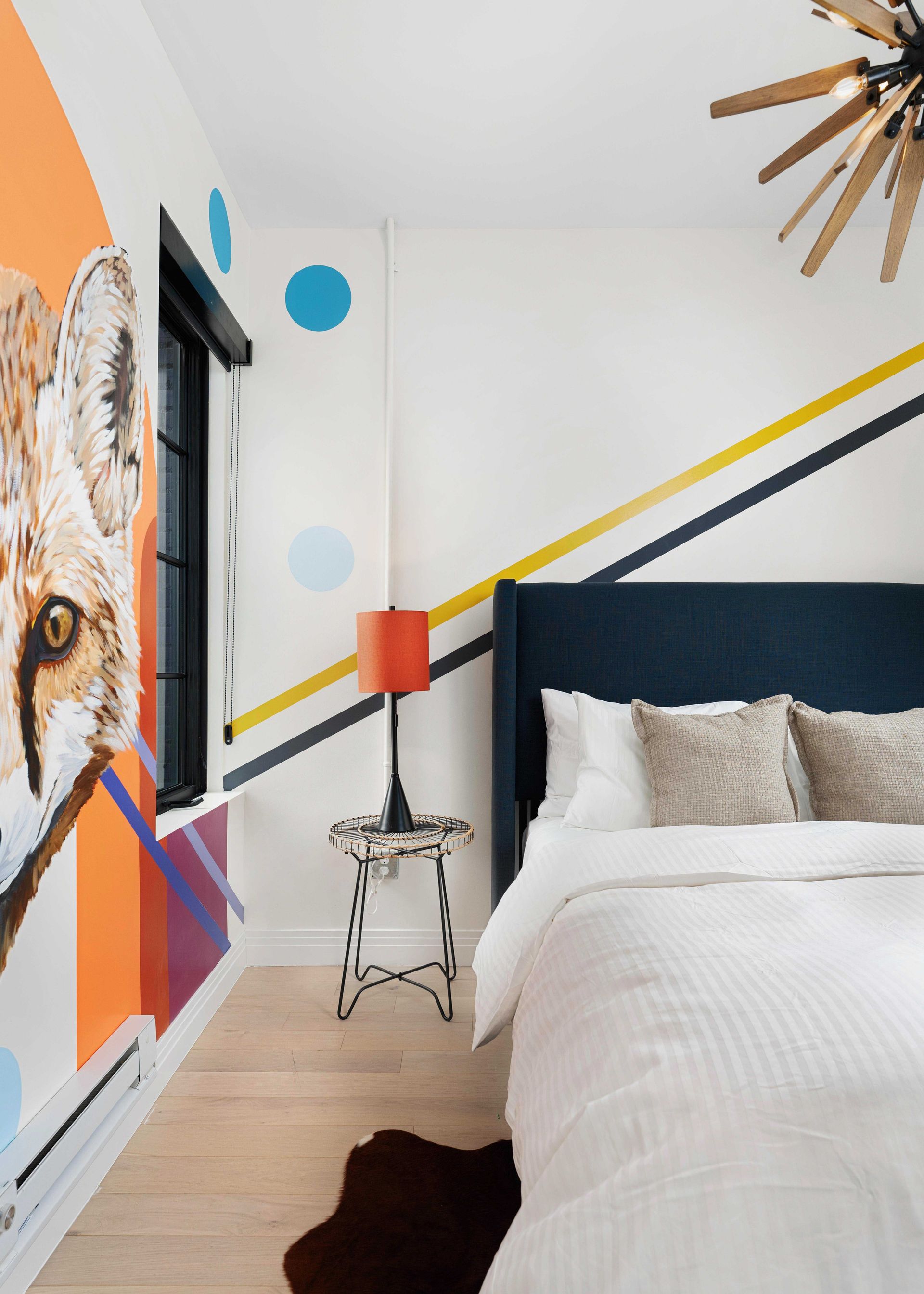 Modern bedroom with white bedding, navy headboard, colorful wall art, and striped accent wall.