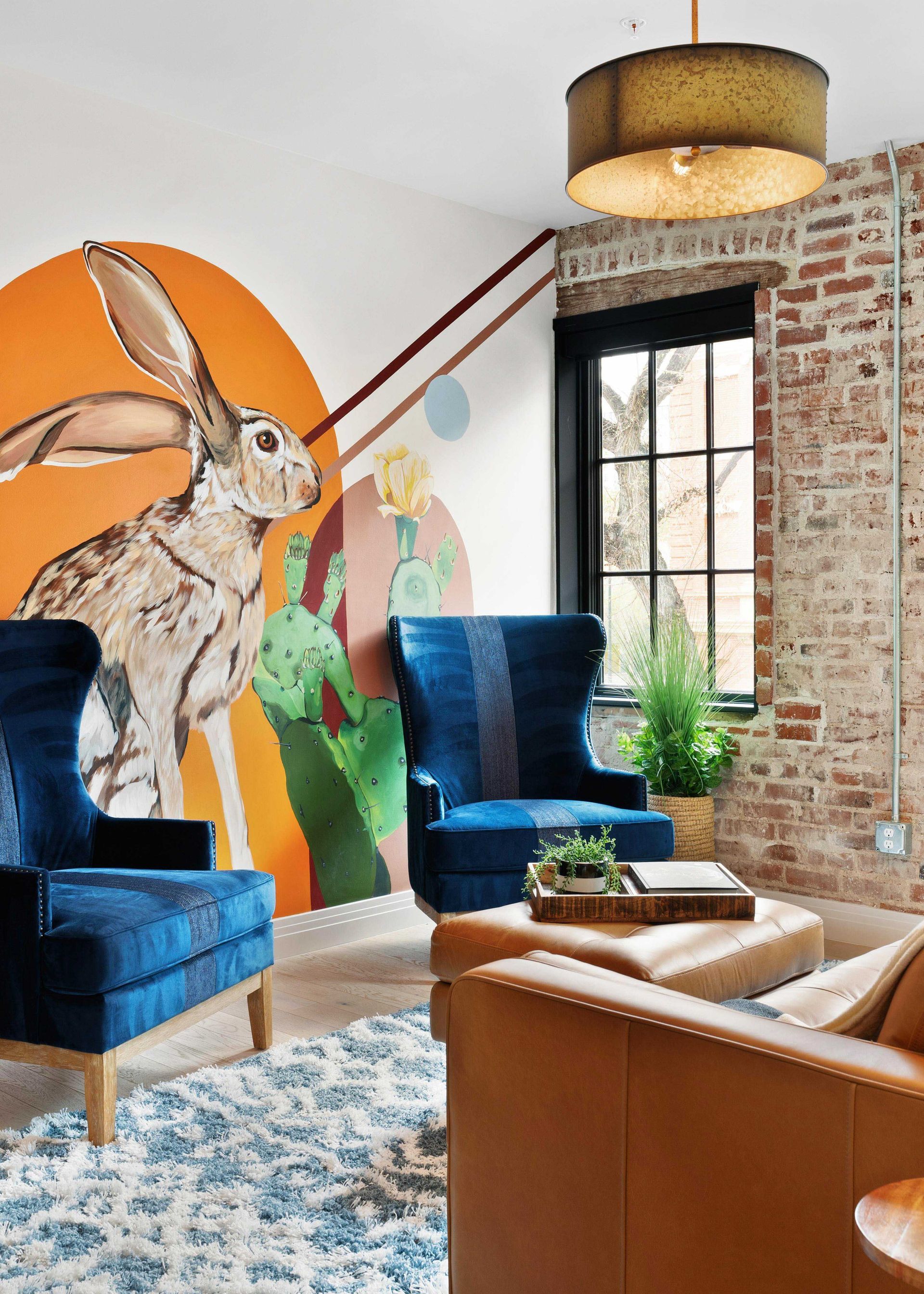 Stylish living room with rabbit mural, blue chairs, tan leather chair, and exposed brick wall