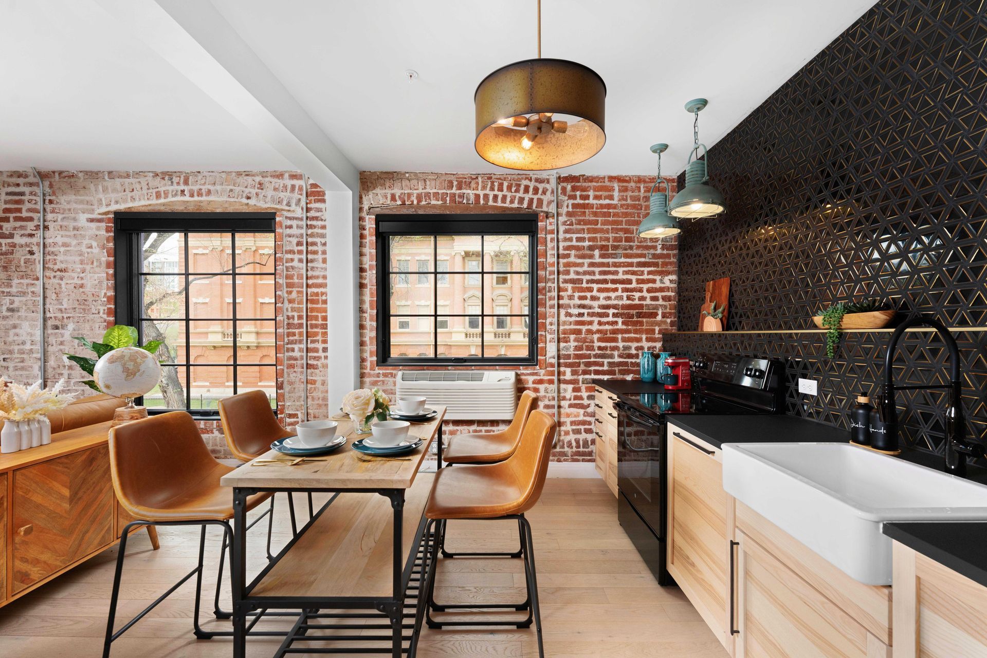 Modern kitchen and dining area with exposed brick, black cabinets, wood table, and large windows