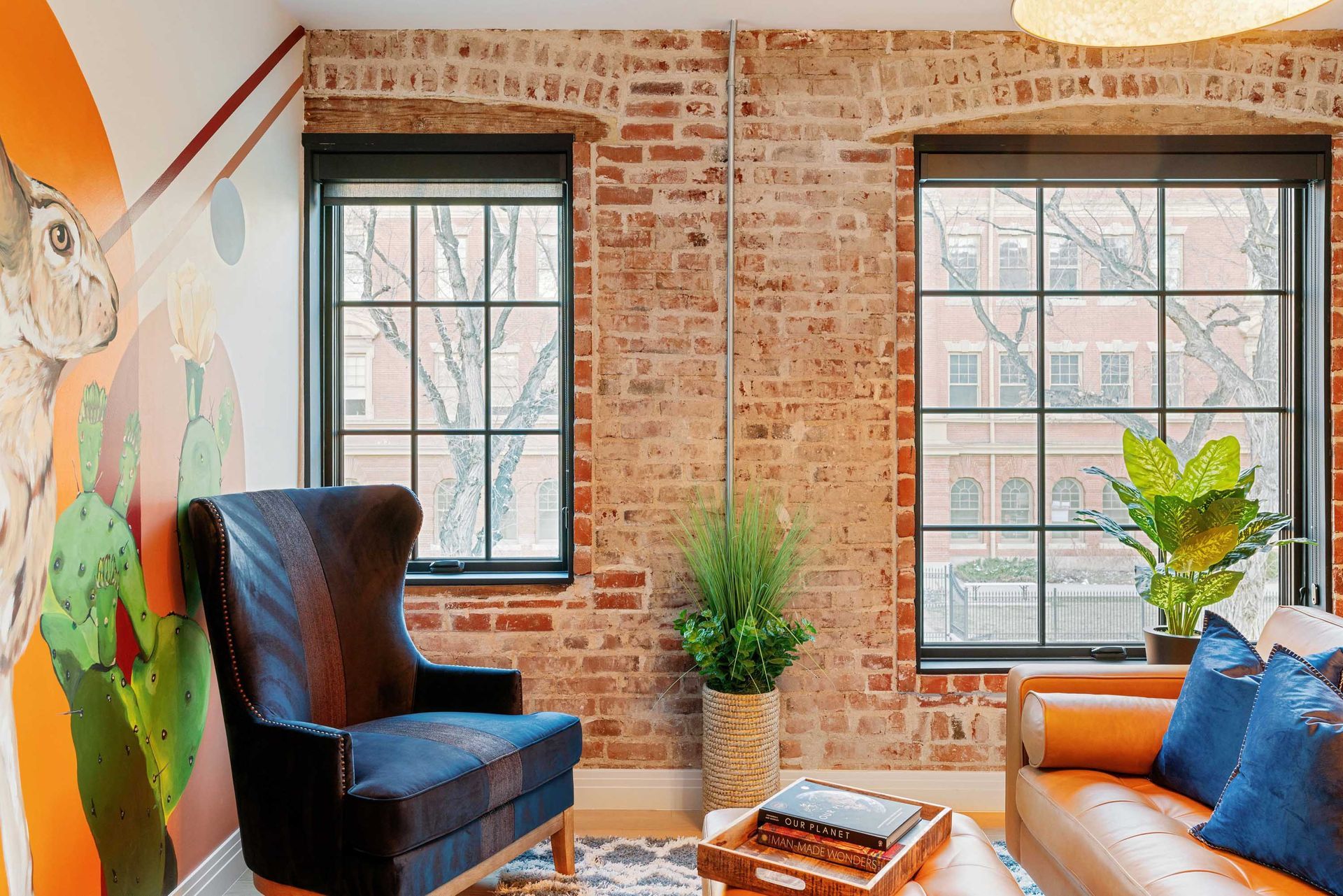 Cozy loft living room with exposed brick, two windows, a black chair, orange sofa, and potted plants