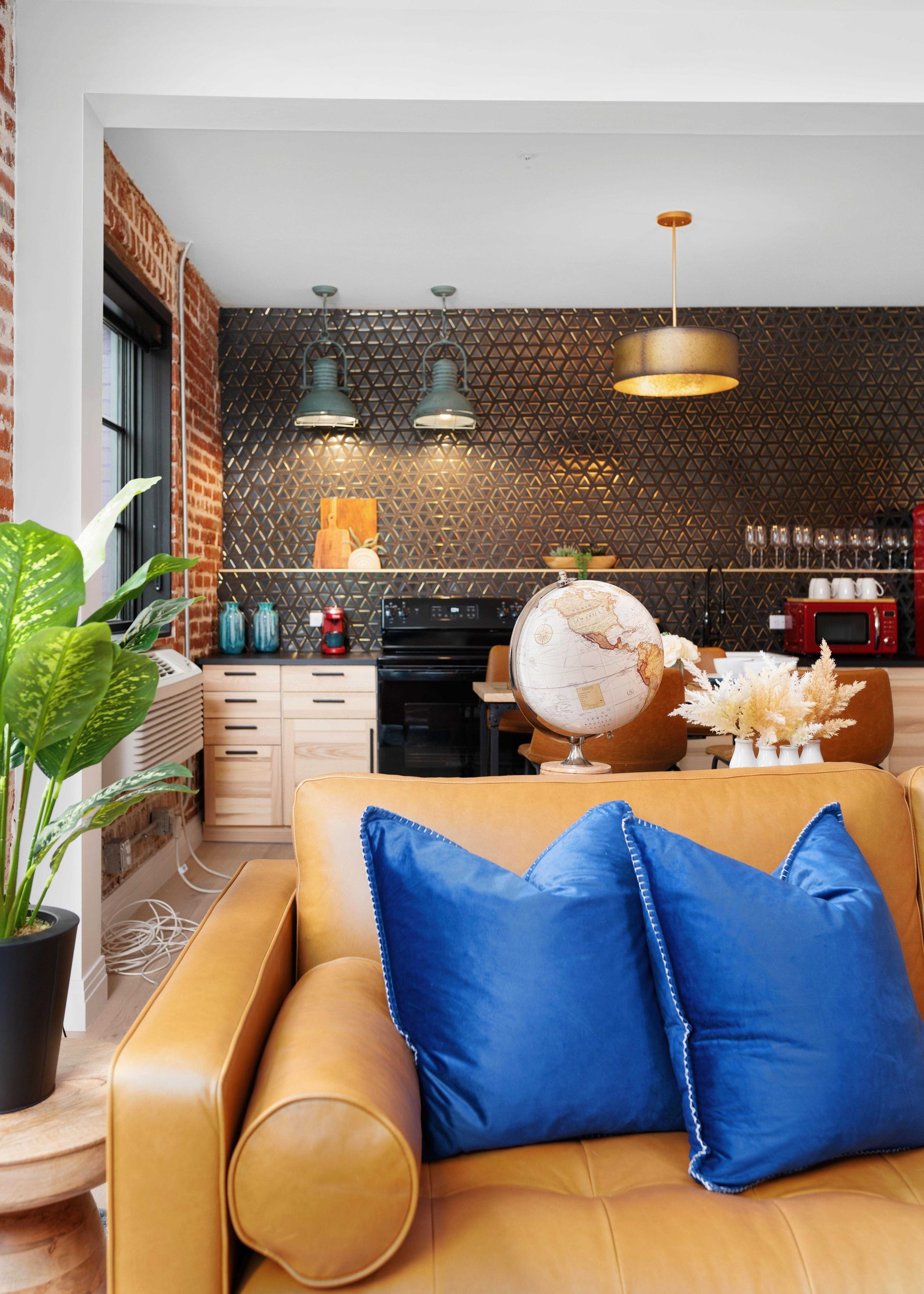 Modern kitchen with brick wall, pendant lights, tan sofa, blue pillows, and globe on a table