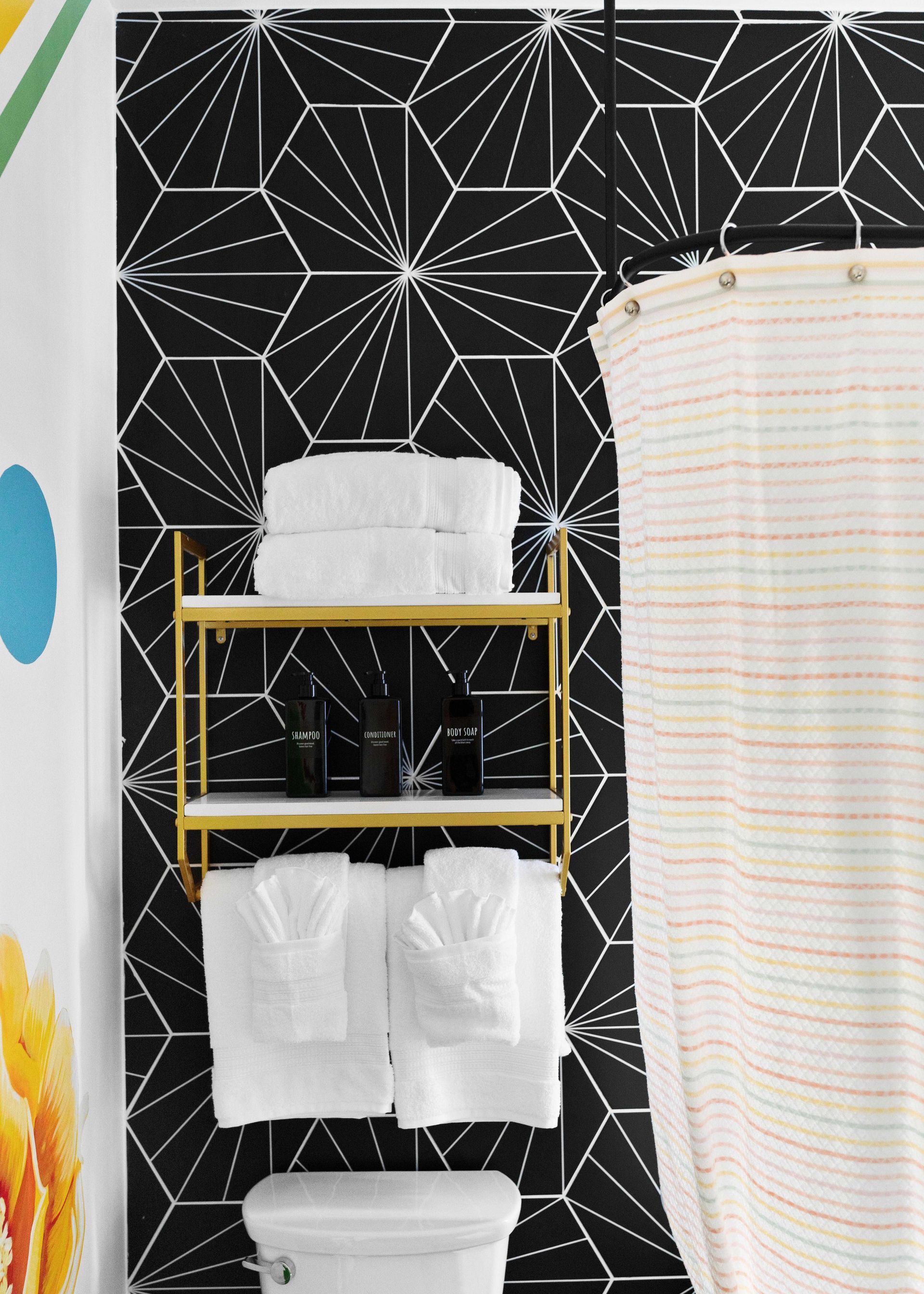 Bathroom shelf with white towels, toilet paper, and a striped shower curtain against black geometric wallpaper