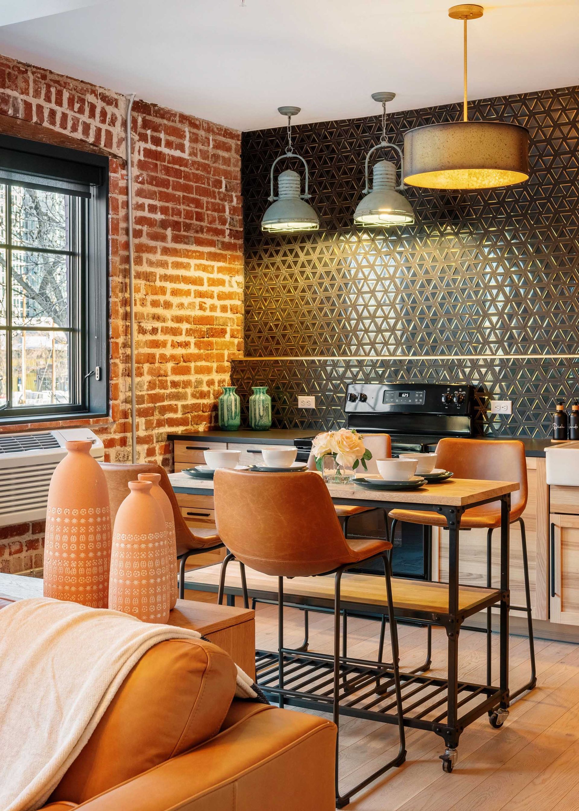 Cozy brick-walled kitchen with black mosaic backsplash, wood table, and tan leather chairs