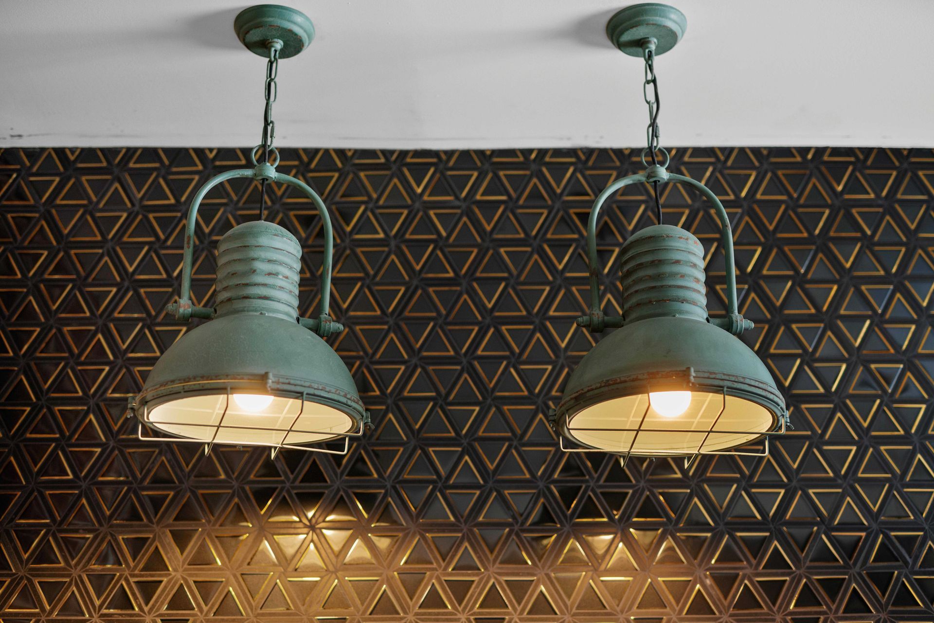 Two hanging green pendant lights against a geometric patterned wall, glowing warmly