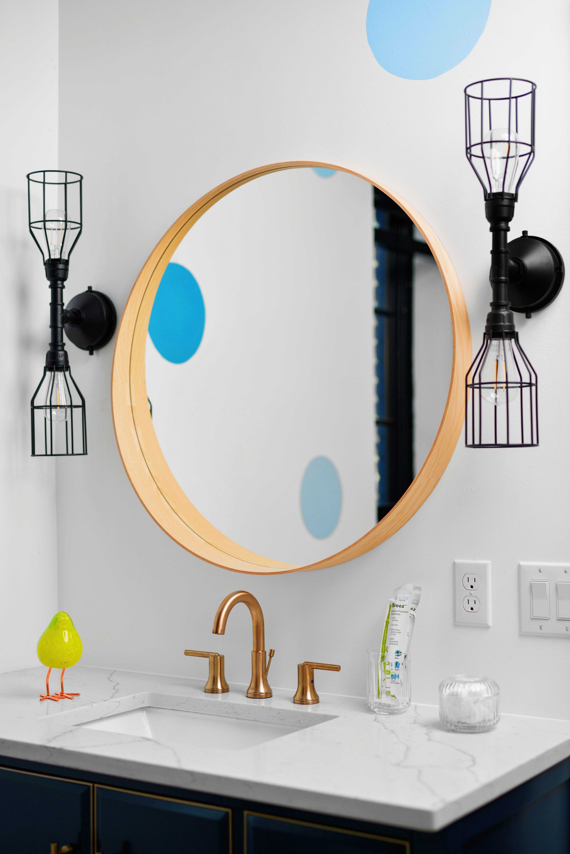 Bathroom vanity with round wood-framed mirror, black wall sconces, white marble sink, and gold faucet