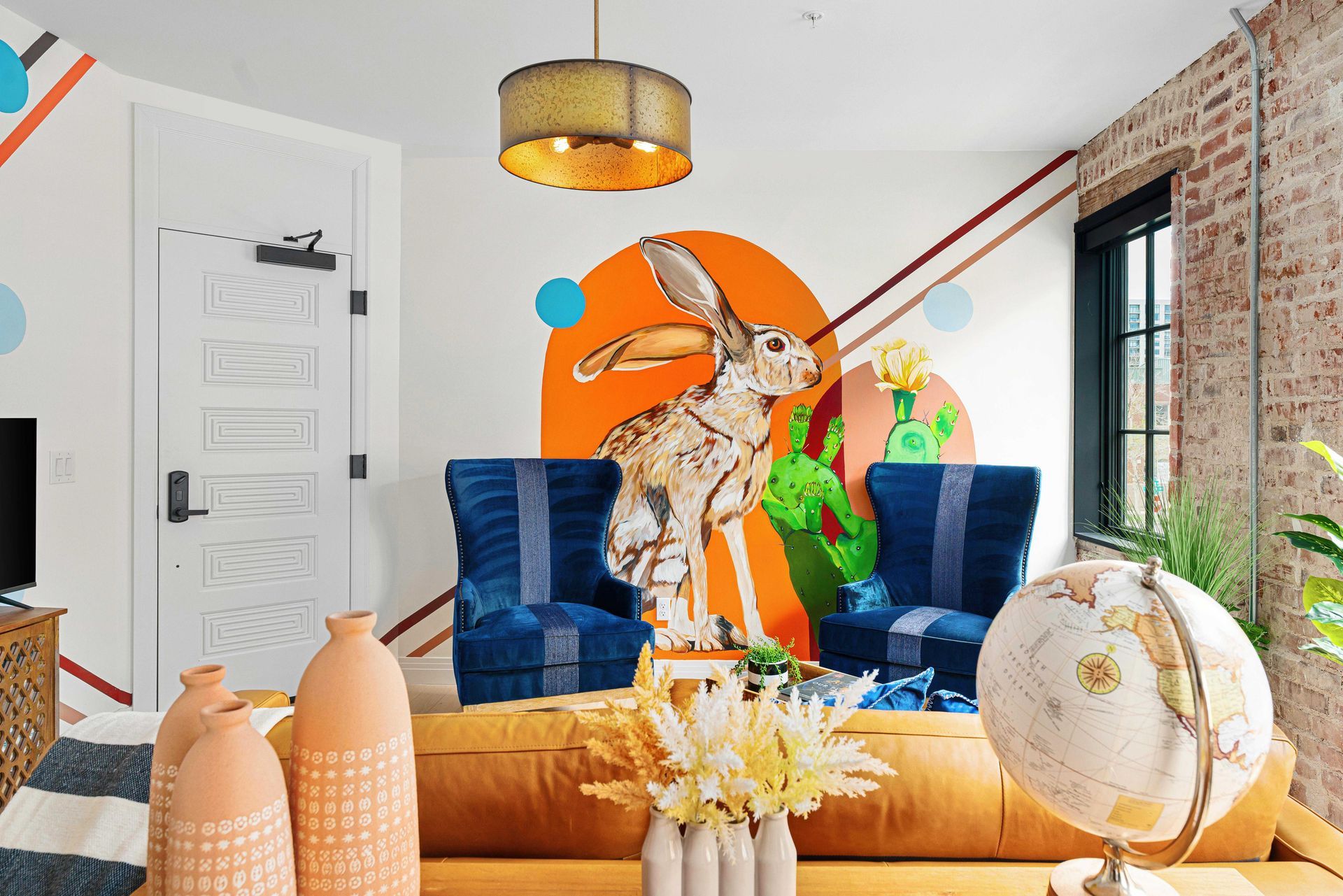 Bright living room with blue chairs, tan sofa, orange wall art, and a globe in the foreground