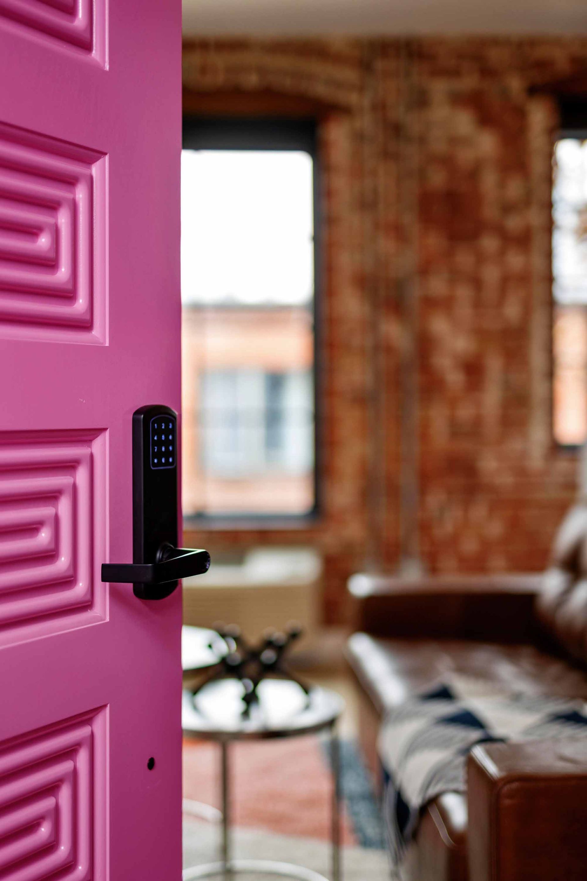 Open pink door revealing a blurred living room with brick walls and a leather couch