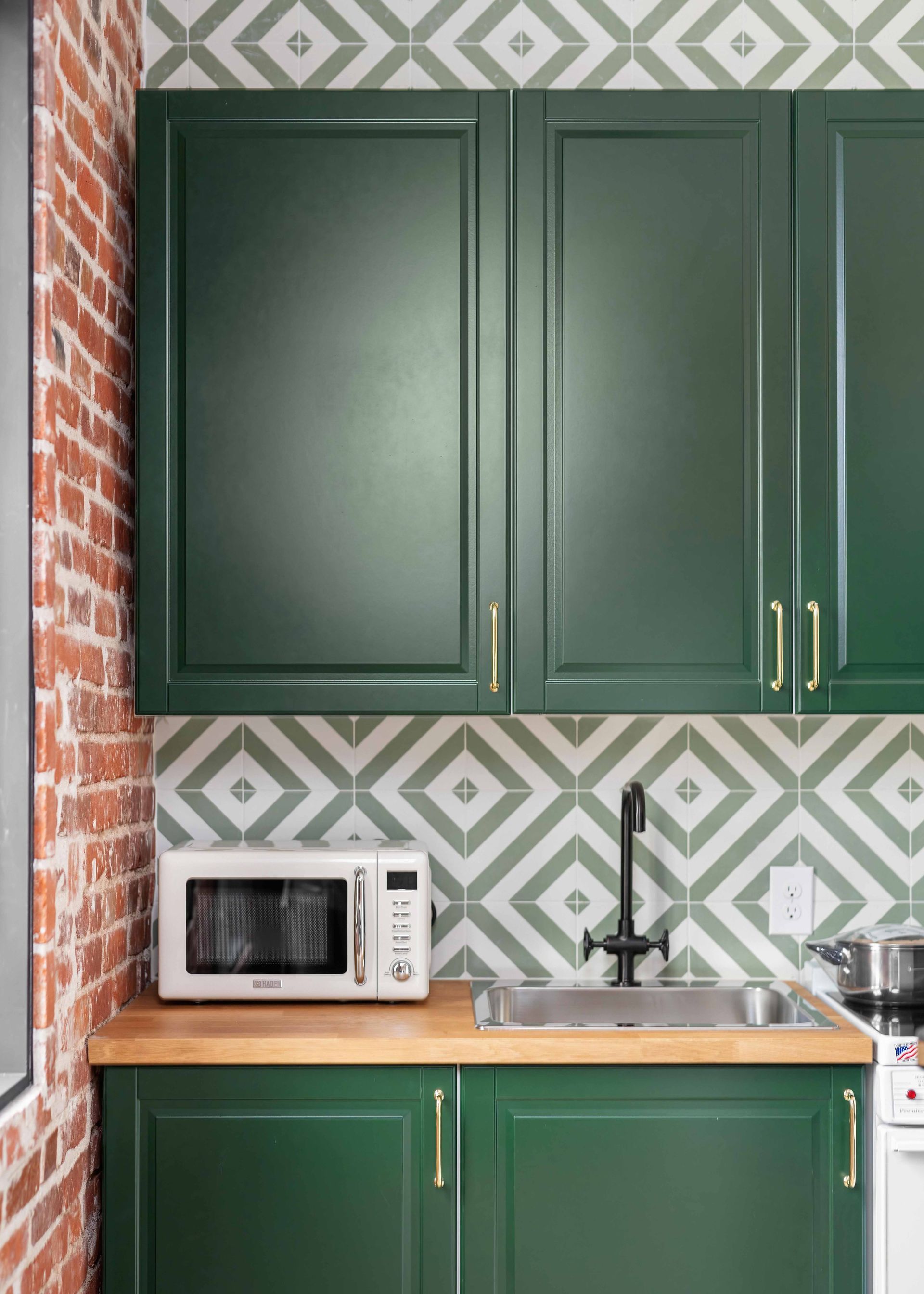 Small kitchen with dark green cabinets, geometric backsplash, sink, and a microwave on the countertop.
