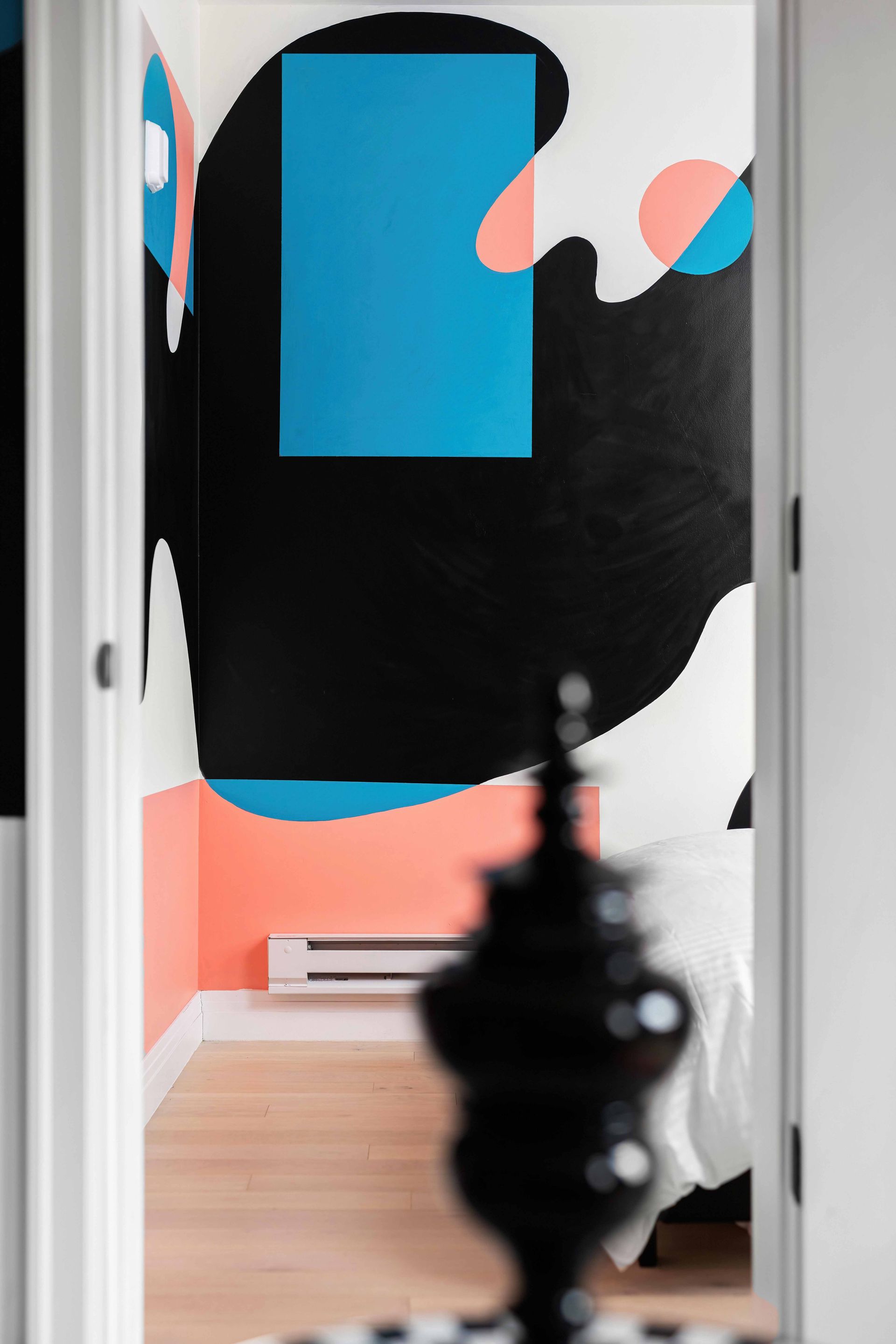 Abstract black, coral, and blue wall art in a doorway, with a blurred dark sculpture in the foreground.