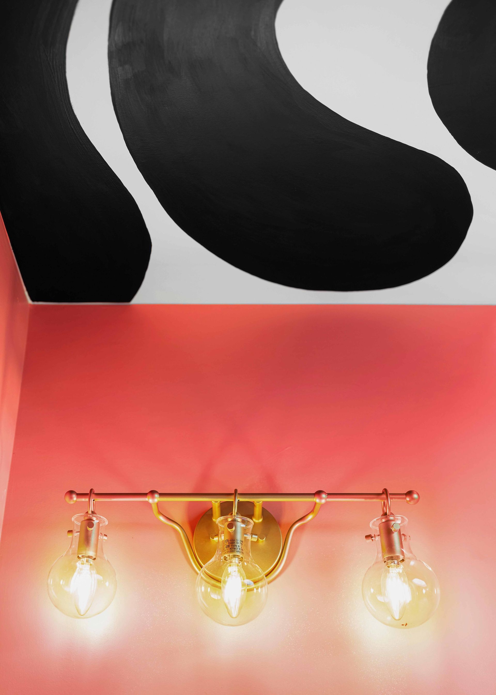 Three lit wall sconces below black-and-white abstract wall art on a pink wall