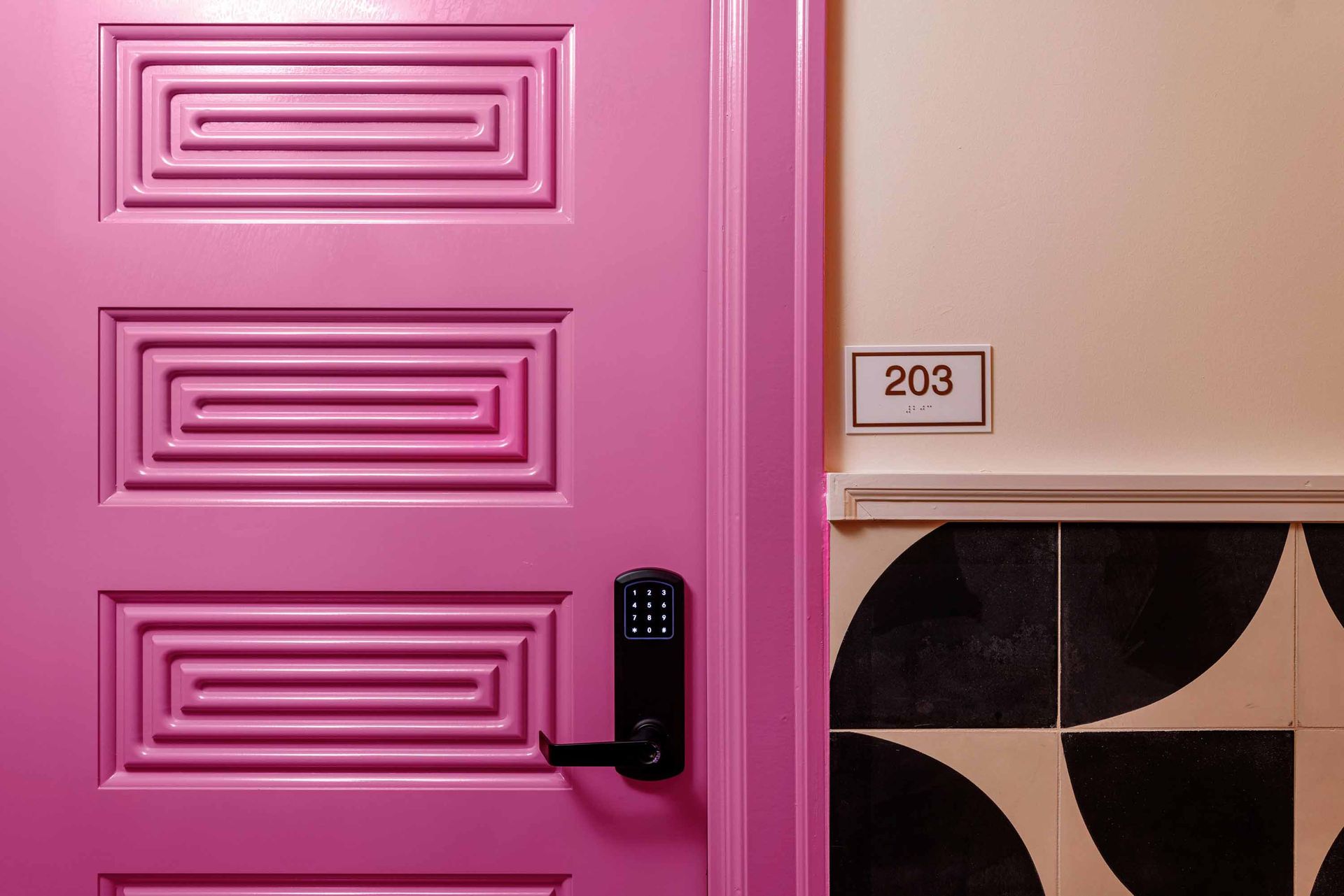 Pink door with black keypad lock beside room number 203 and patterned wall tiles
