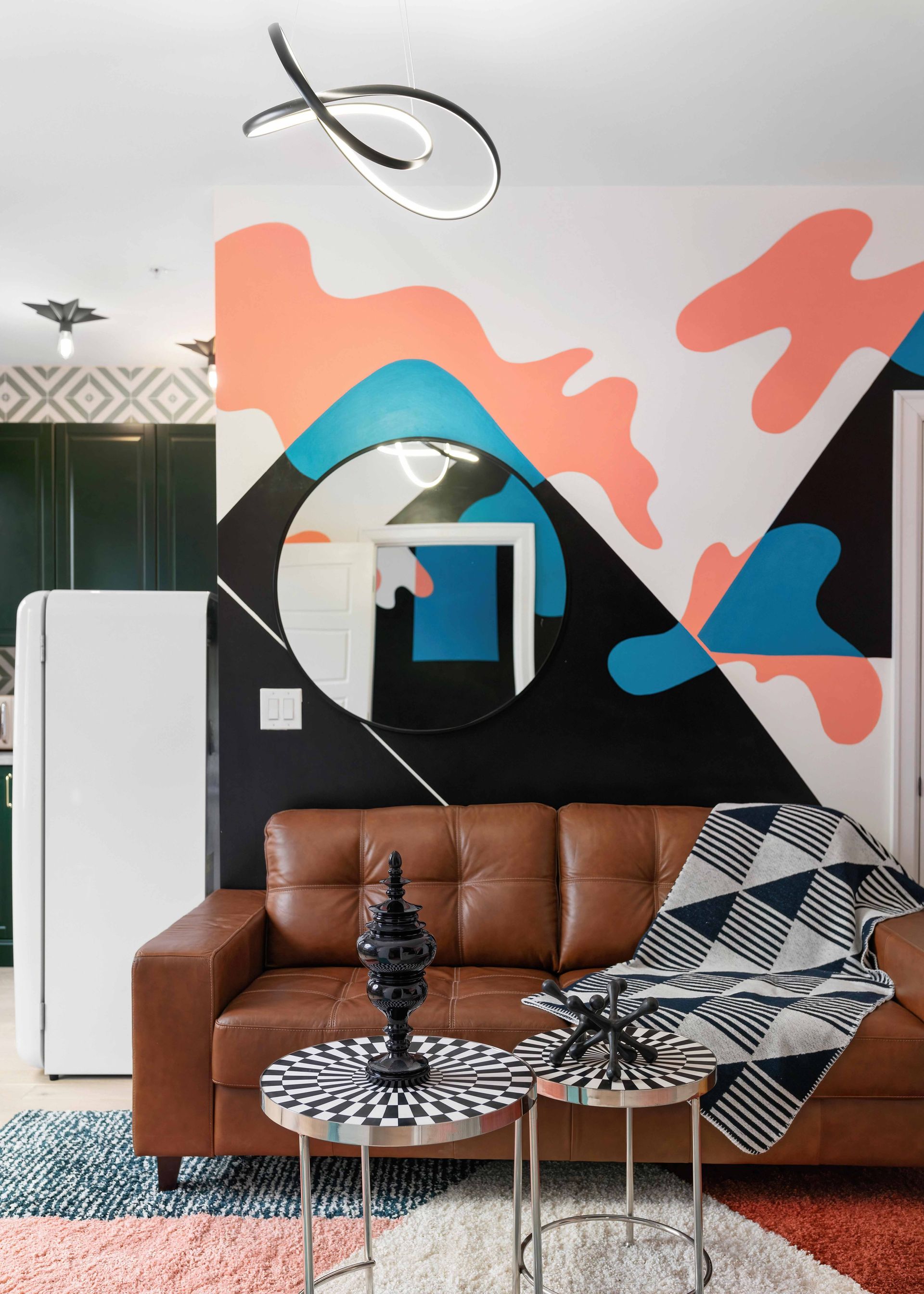 Modern living room with brown sofa, geometric mural, patterned chairs, and black-and-white decor