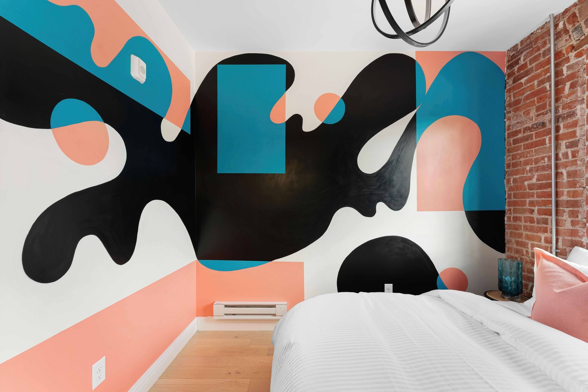 Modern bedroom with abstract black, teal, and peach mural on the wall above a white bed