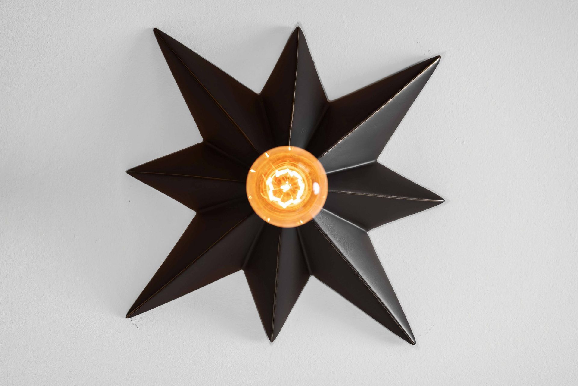 Black star-shaped decorative object with an orange center on a light gray wall