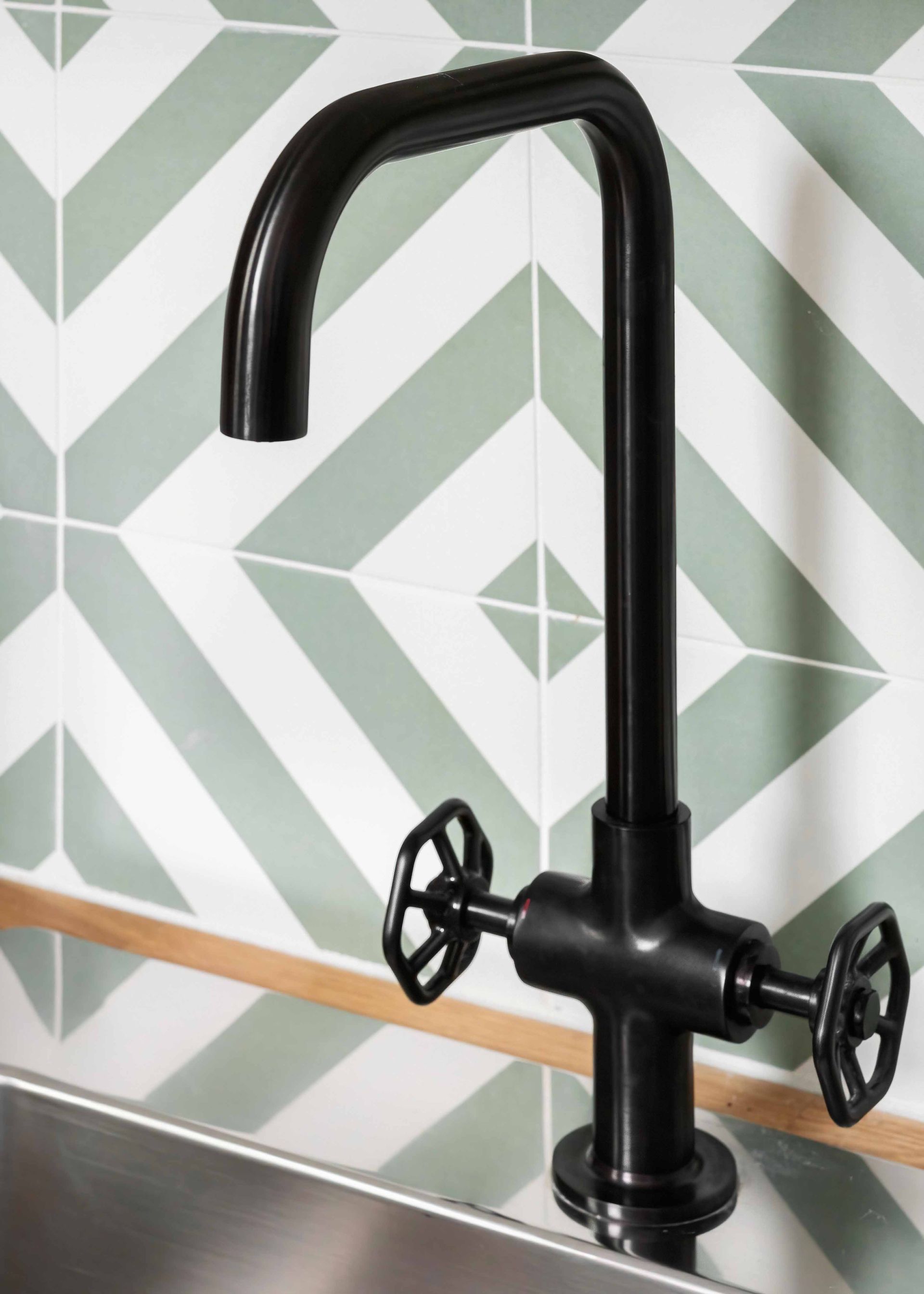 Black kitchen faucet with two cross handles against a green-and-white geometric tile wall