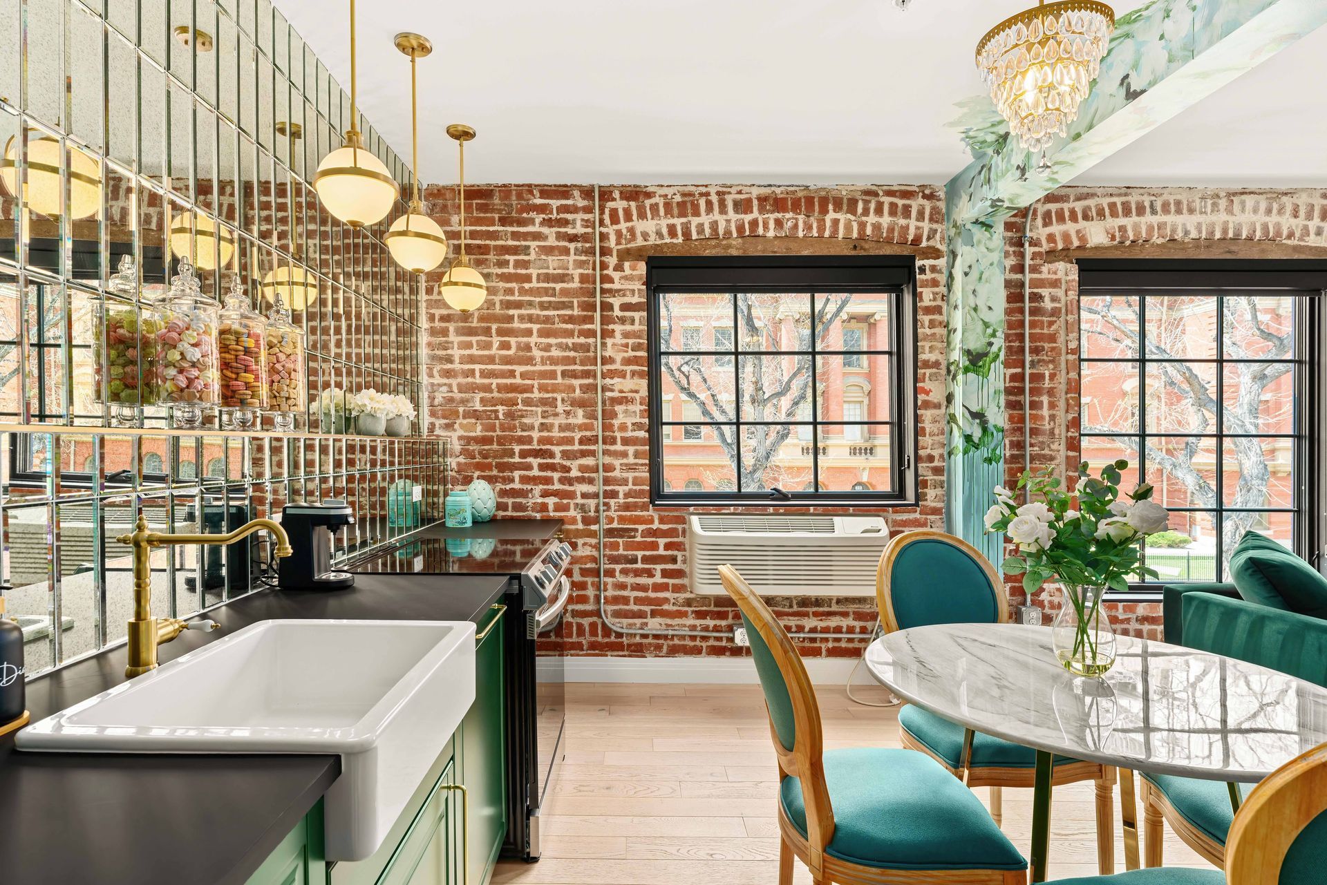 Bright café interior with brick walls, brass lights, a white sink, and teal chairs by a marble table