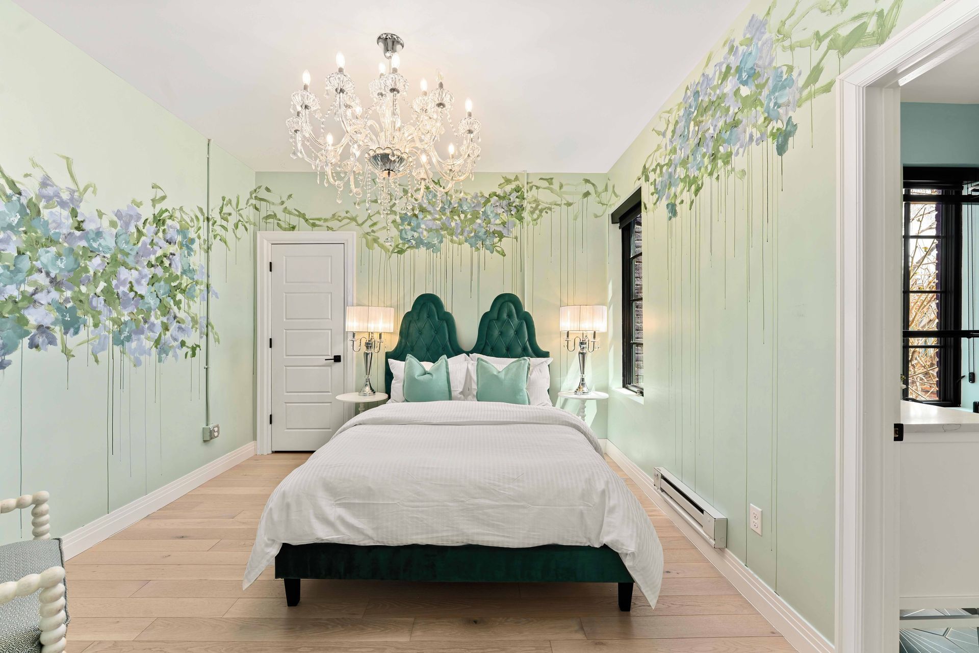 Elegant pastel bedroom with floral wall murals, chandelier, and a neatly made bed