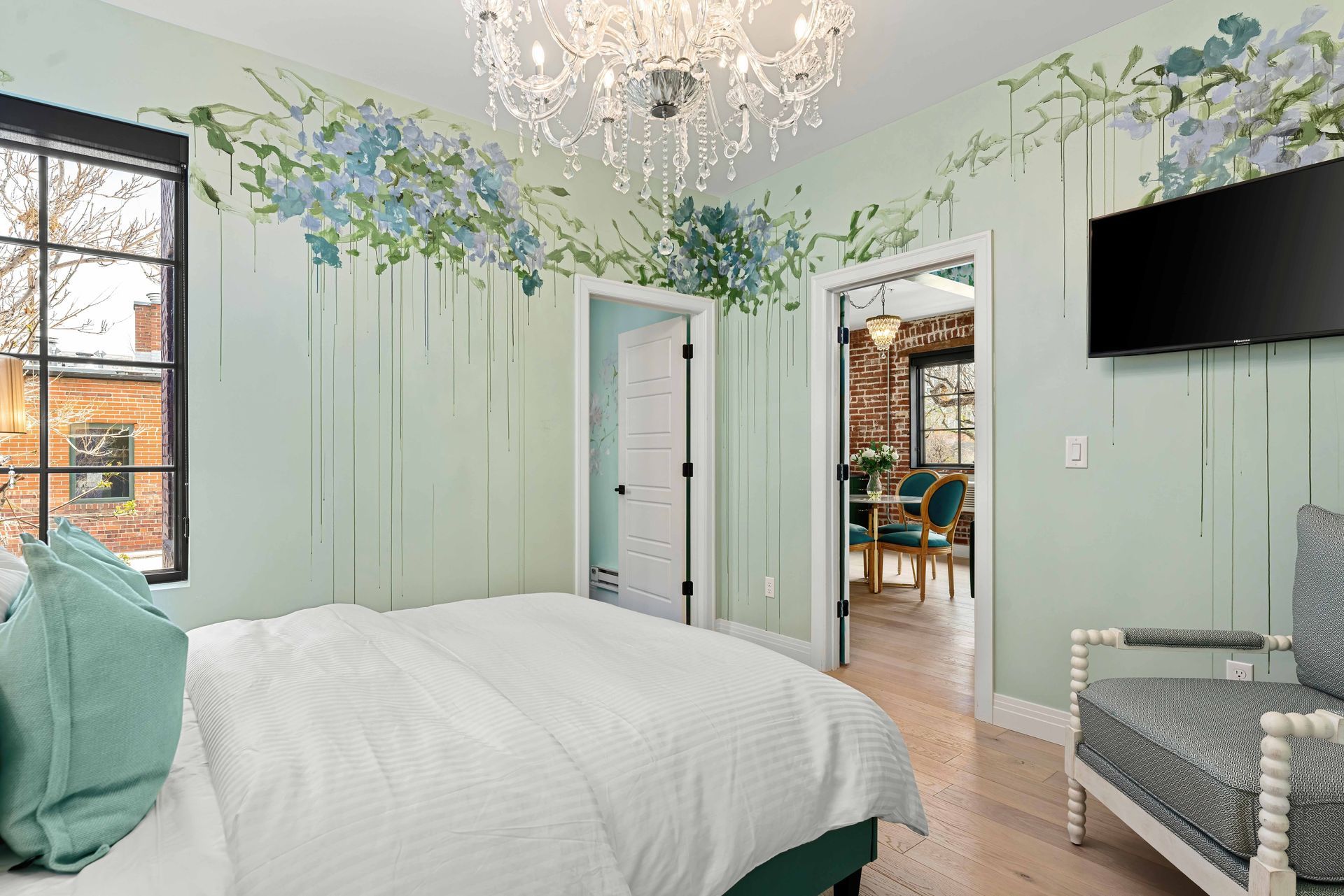 Mint-green bedroom with floral wall mural, white bed, chandelier, and wall-mounted TV