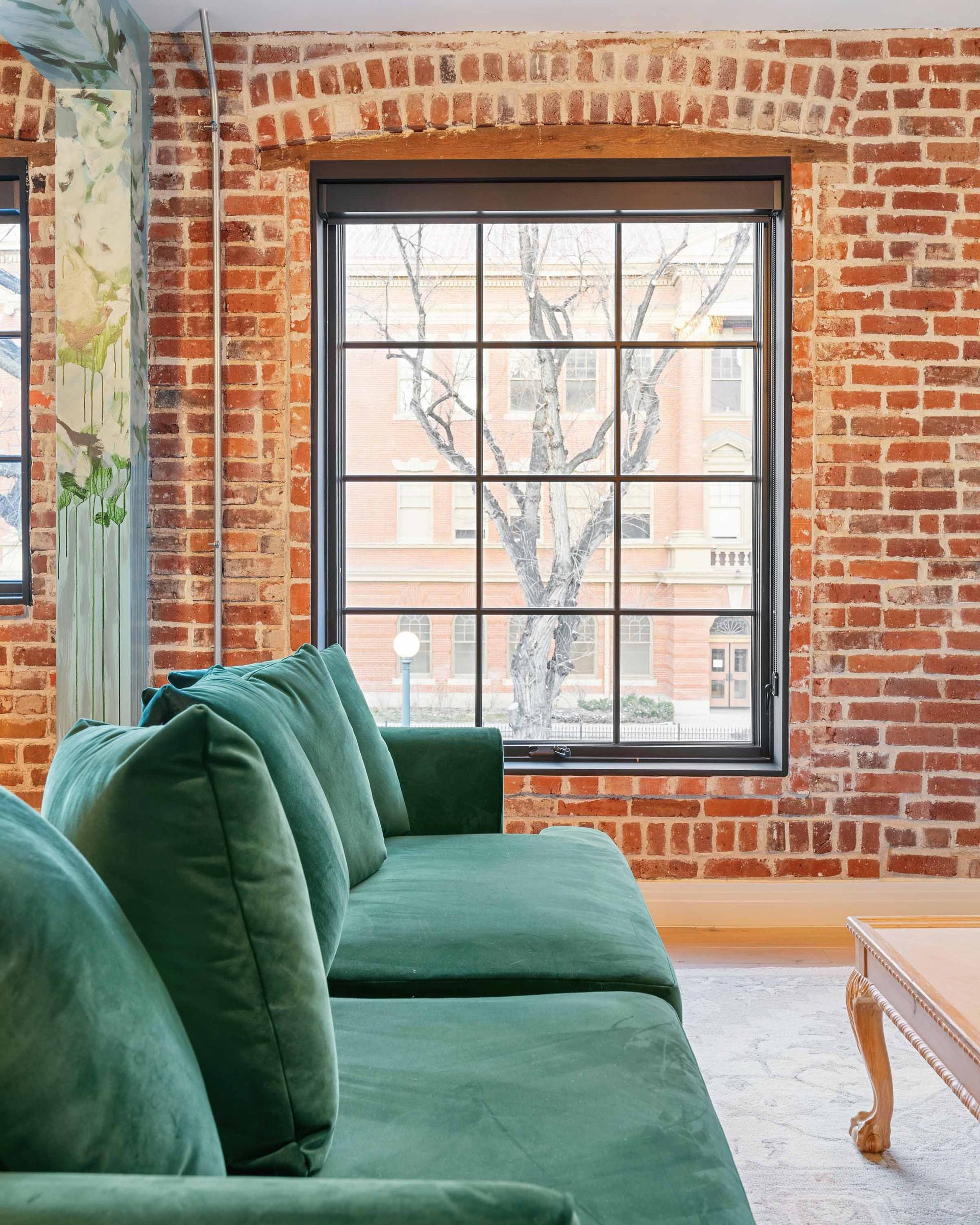 Green velvet sofa in a brick-walled room with a large window and wooden coffee table