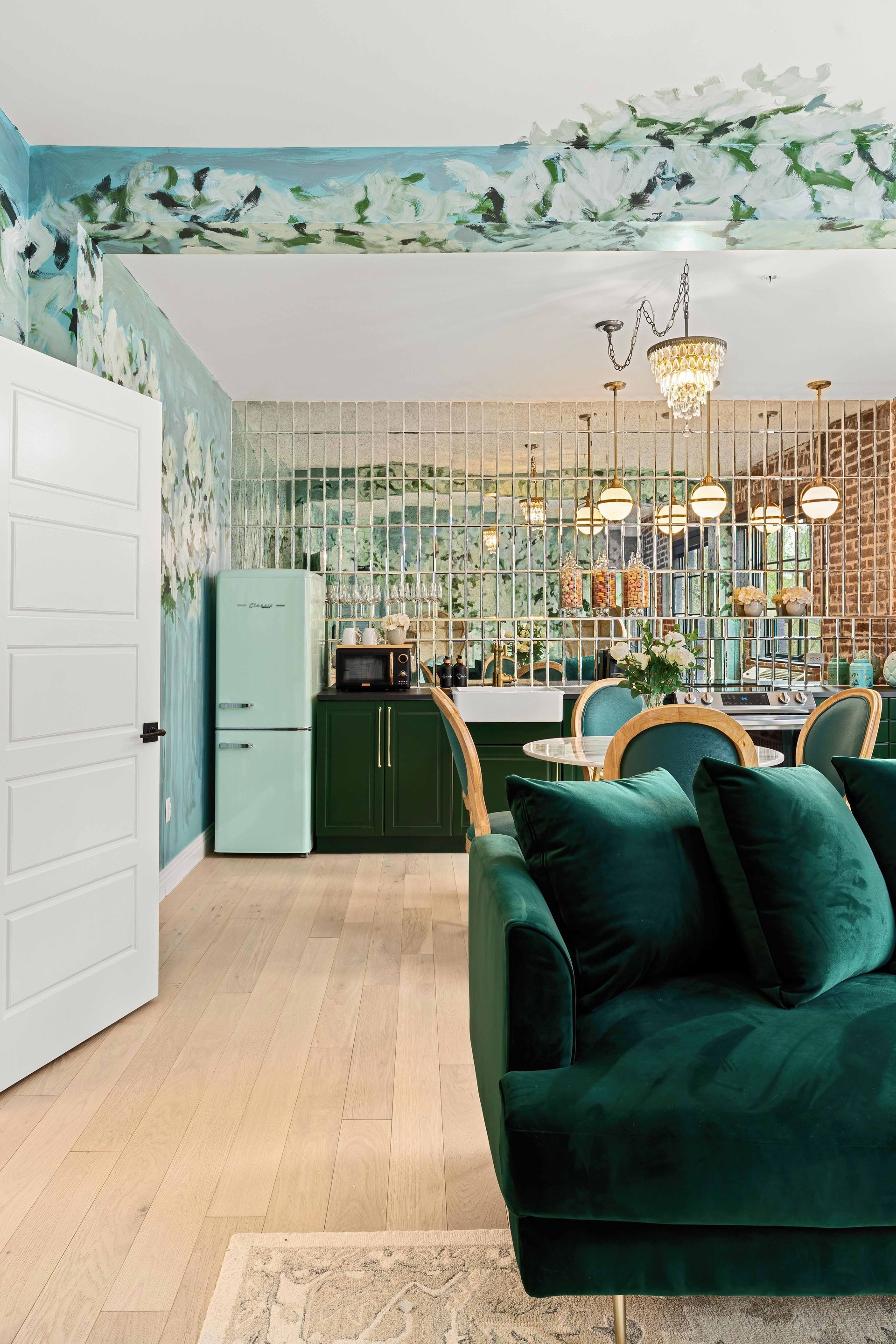 Bright living room with emerald sofa, chandelier, and floral wallpaper leading to a dining area