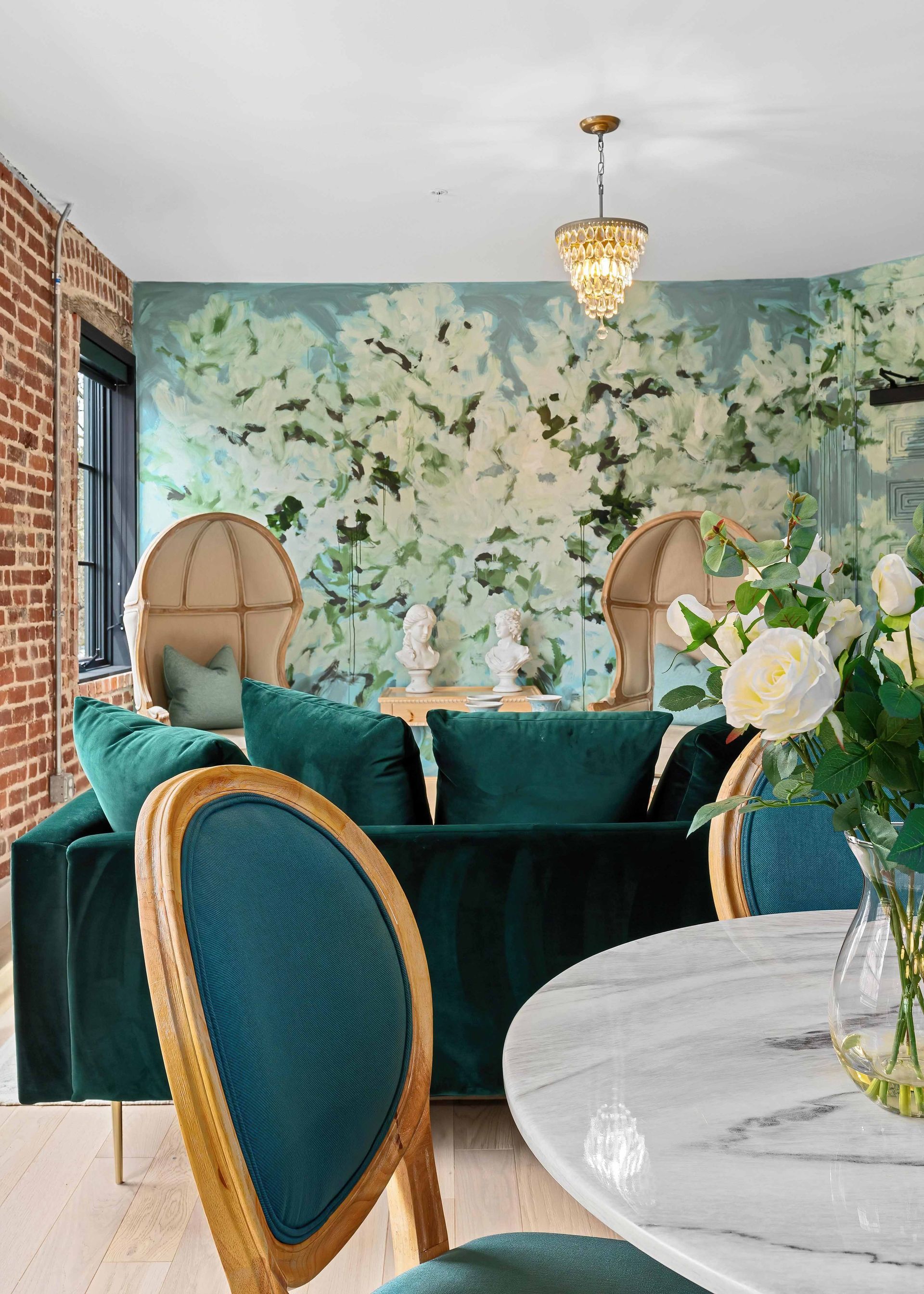 Elegant dining area with teal chairs, marble table, floral wallpaper, and a brass chandelier