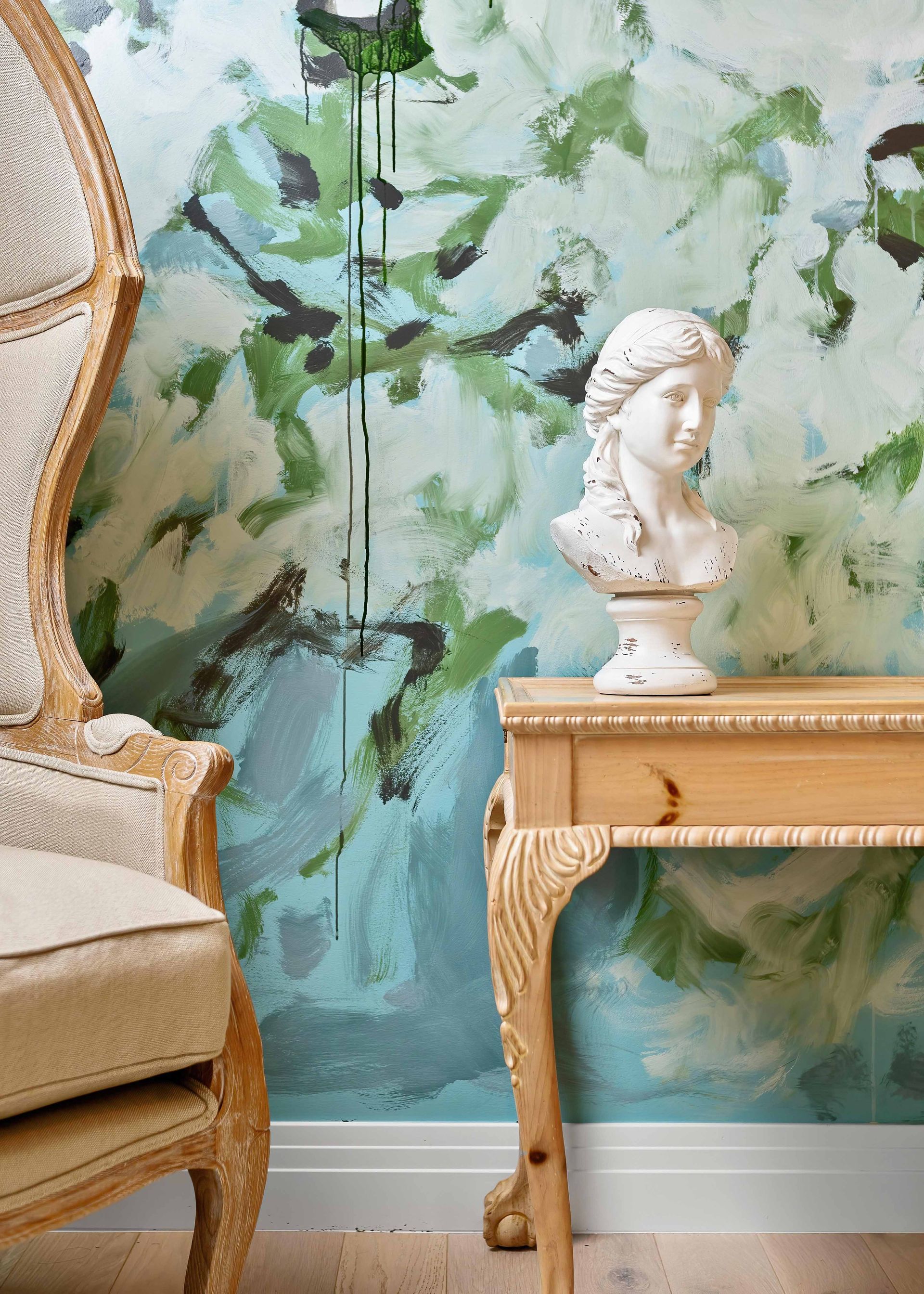 Vintage chair beside a wooden table with white bust against a green floral mural wall
