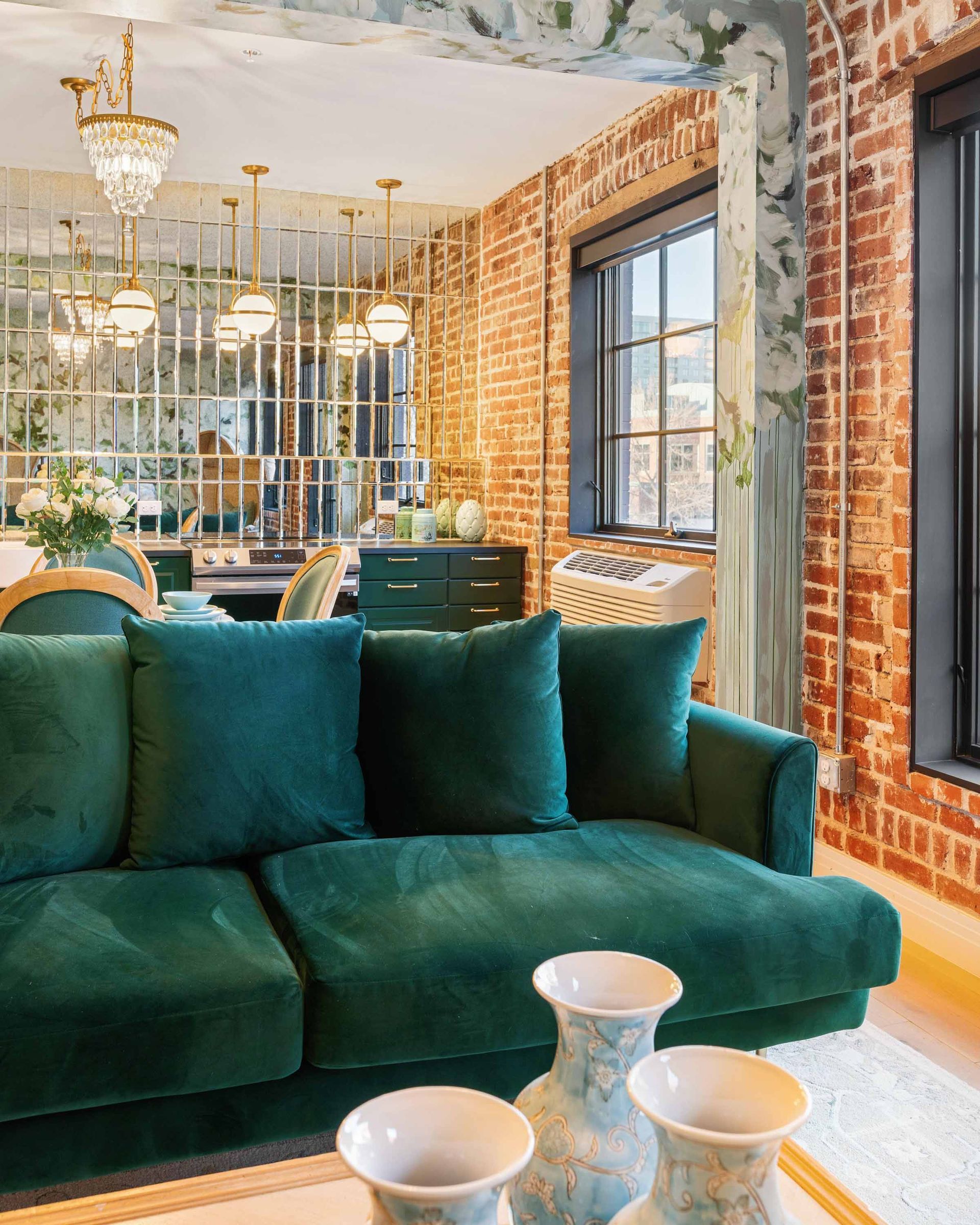 Teal velvet sofa in a stylish brick-walled room with large windows and chandeliers