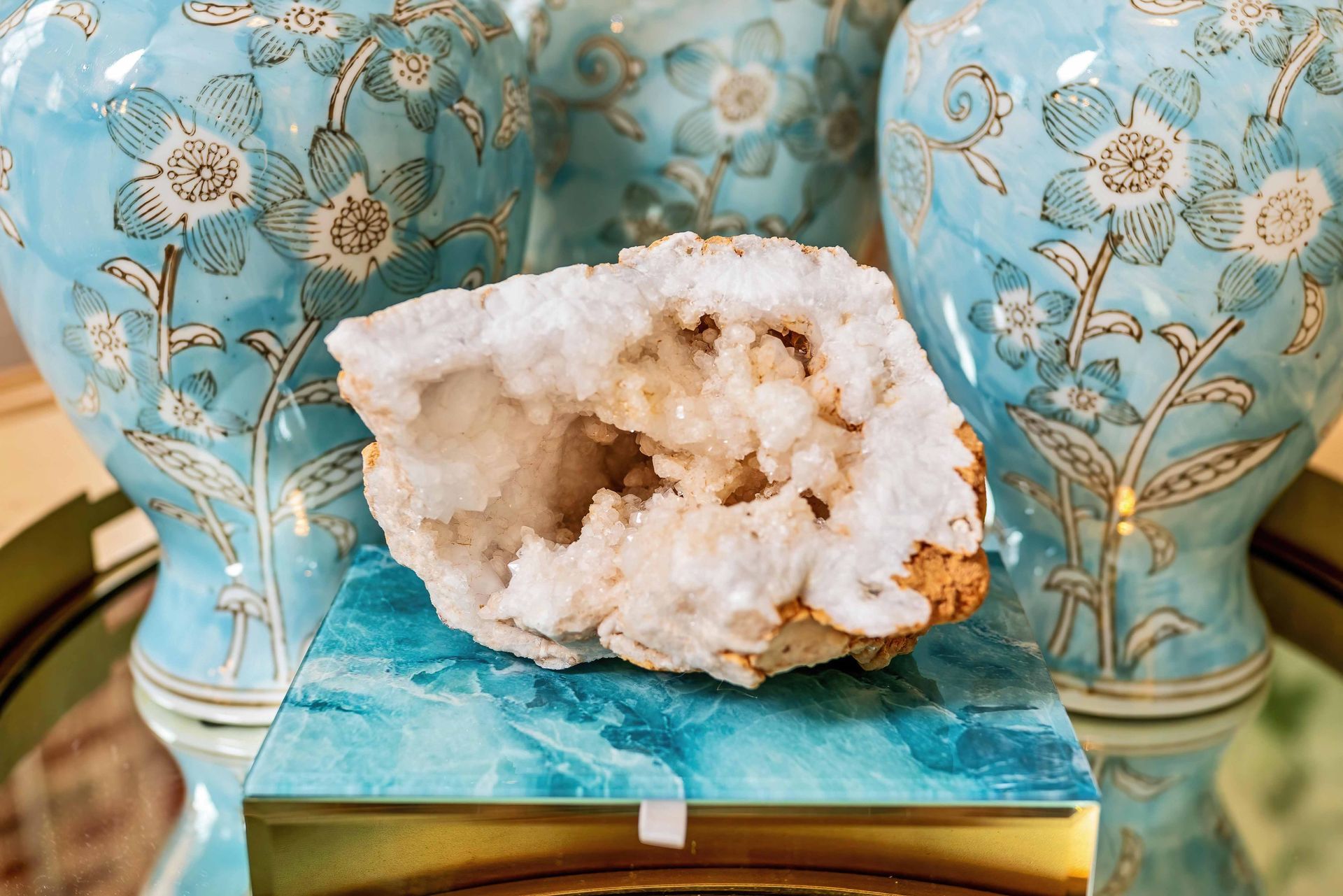 White crystal geode on a blue stand with turquoise floral vases in the background