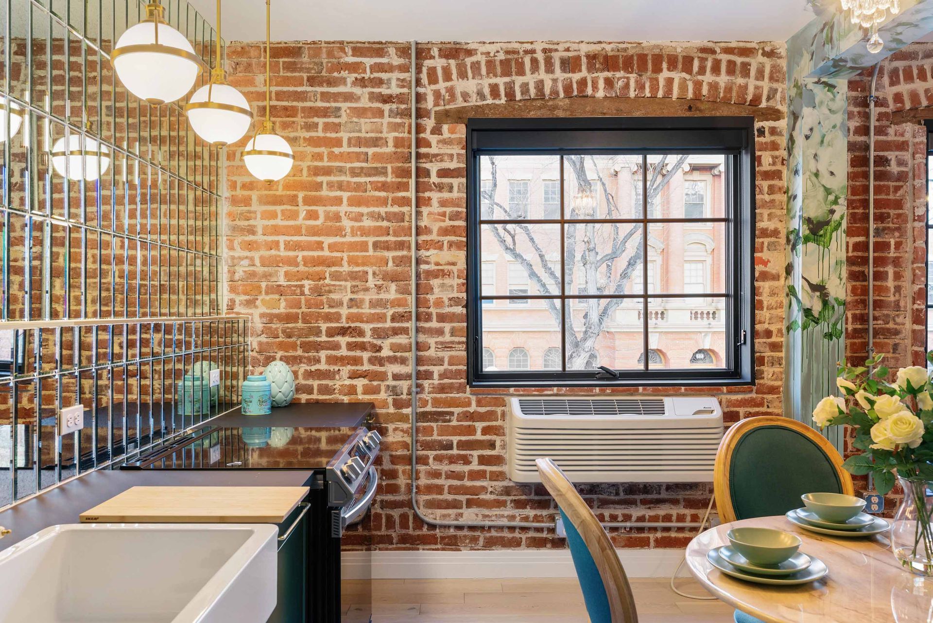 Cozy brick-walled kitchen with a sink, window, round table, and hanging globe lights
