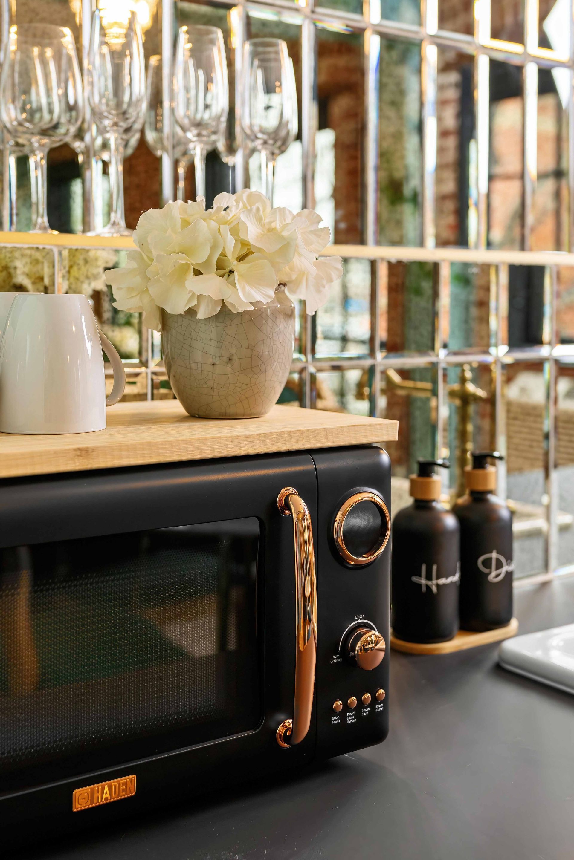Microwave on a countertop beside wine bottles and a vase of white flowers in a bright kitchen or bar area
