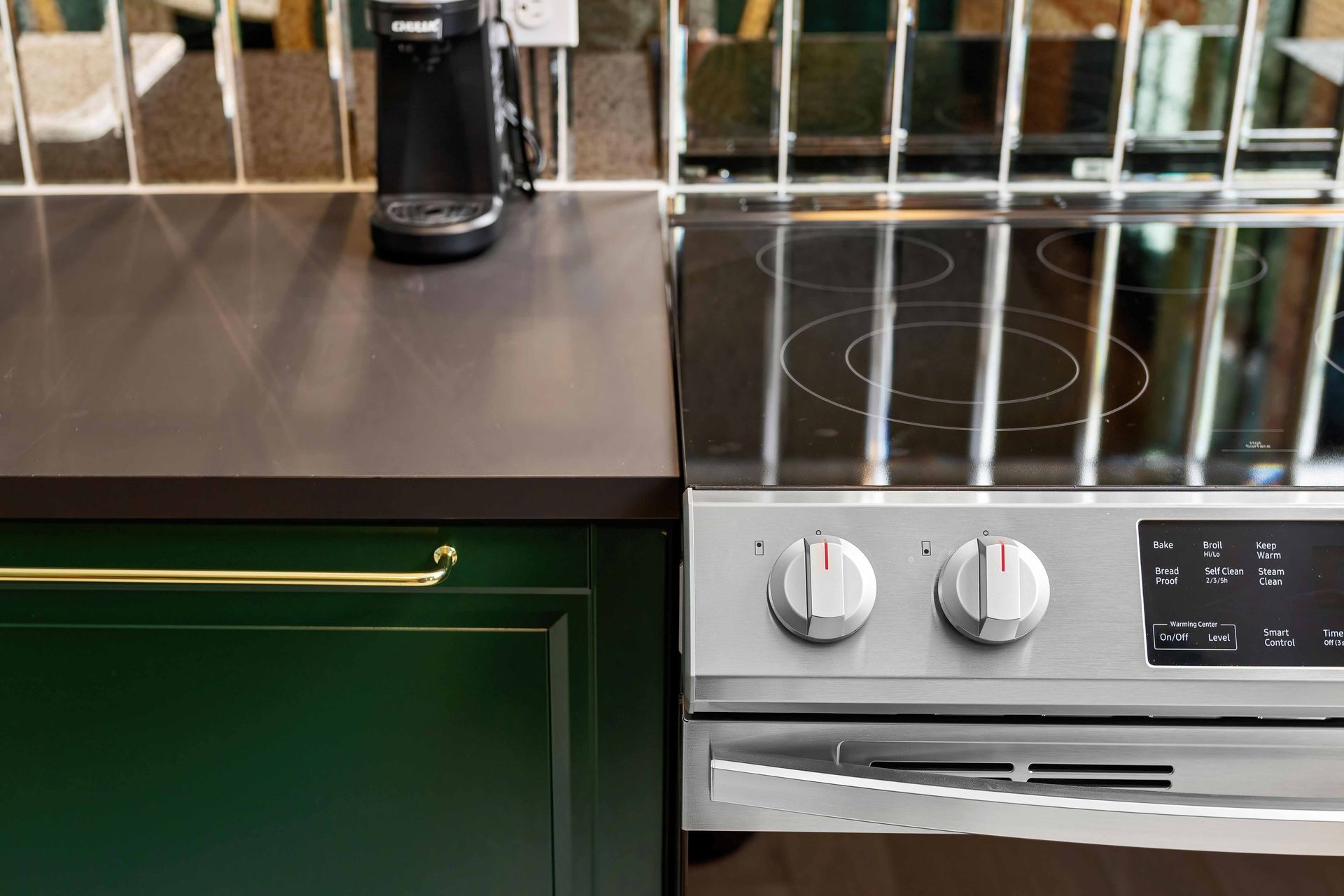Kitchen counter with green cabinets, a black coffee maker, and a stainless steel electric stove.