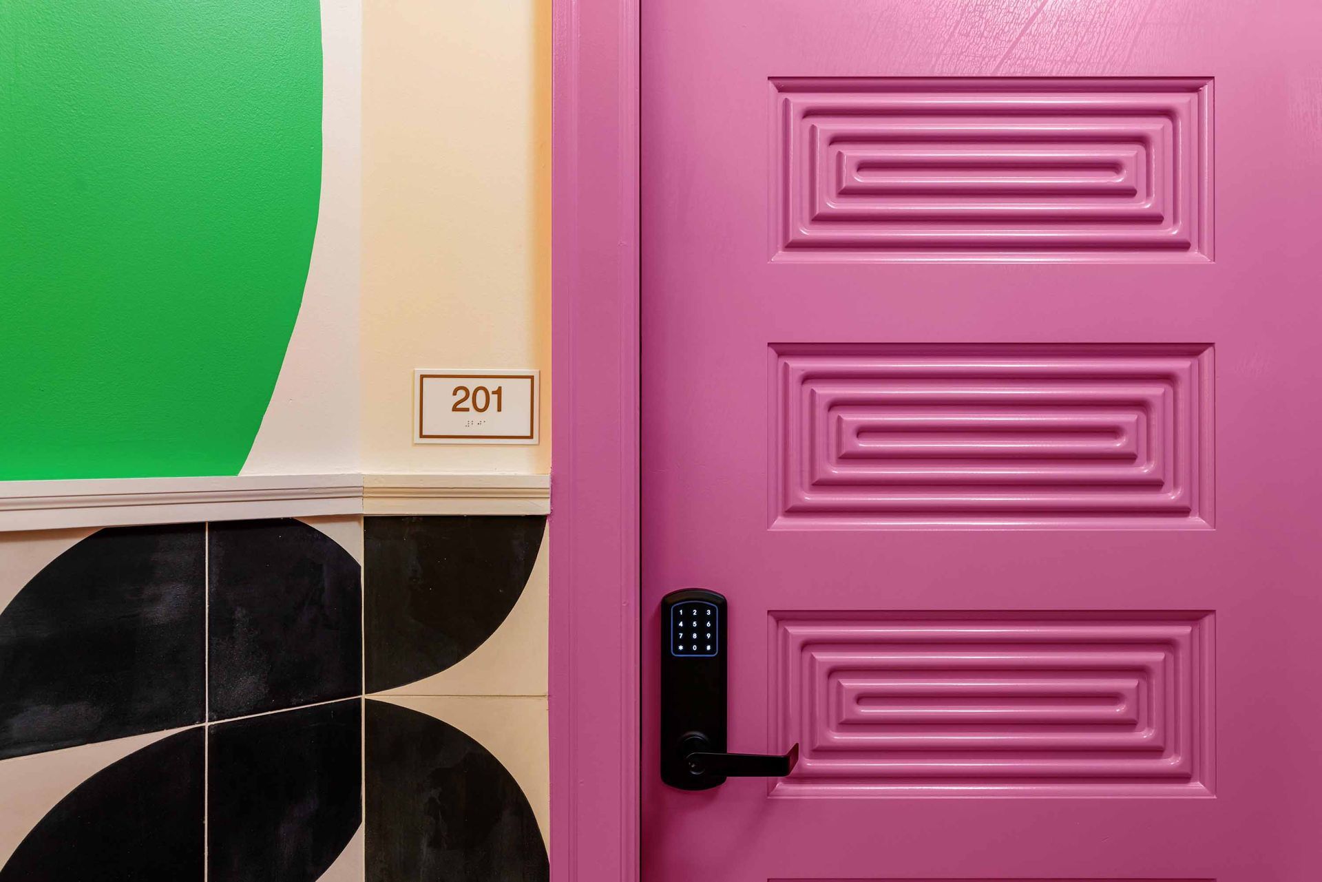 Pink door with black handle beside green and cream wall tiles and black-and-white floor tiles