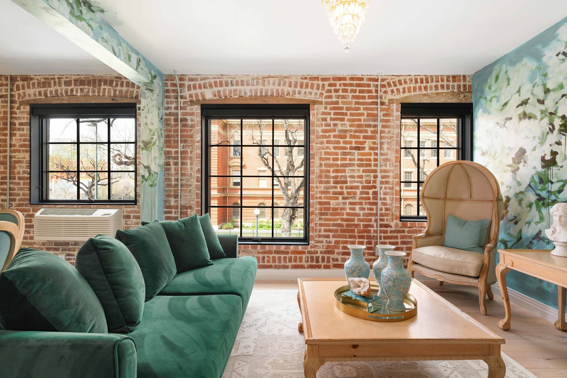 Bright living room with green sofa, brick walls, large windows, and floral mural decor