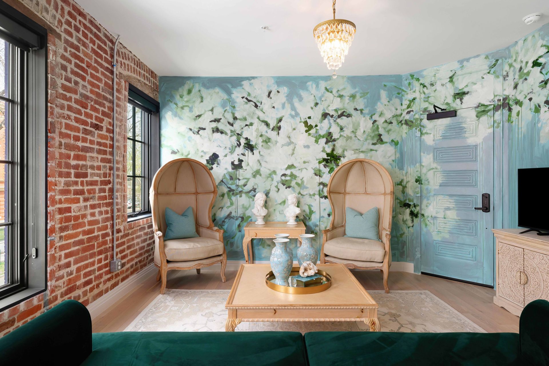 Bright lounge with floral wallpaper, wicker chairs, teal couch, and brick accent wall