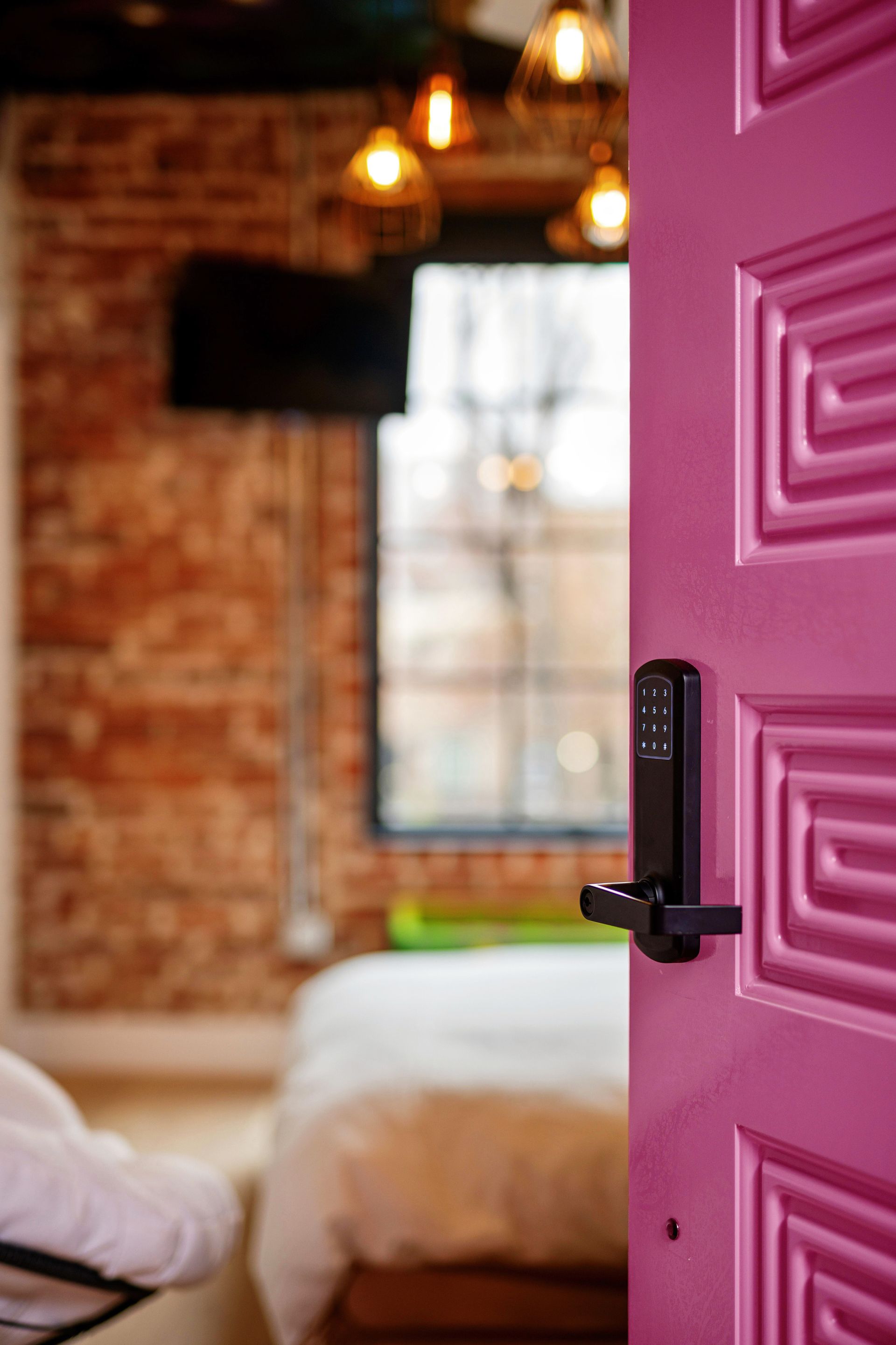 Pink door ajar to a cozy brick-walled bedroom with a bed and hanging lights