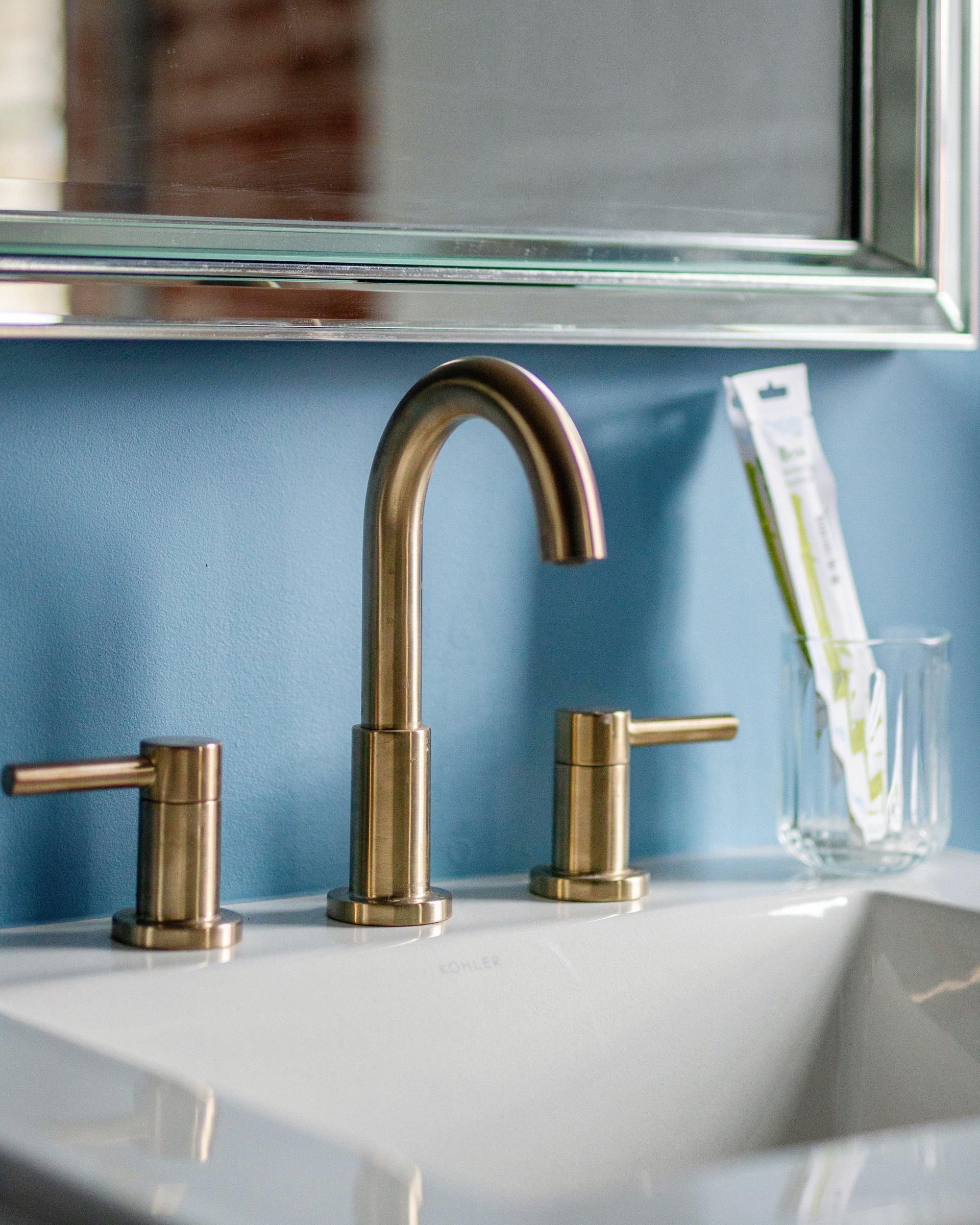 Bathroom sink with brass faucet, soap dispenser, and toothbrush holder under a mirror