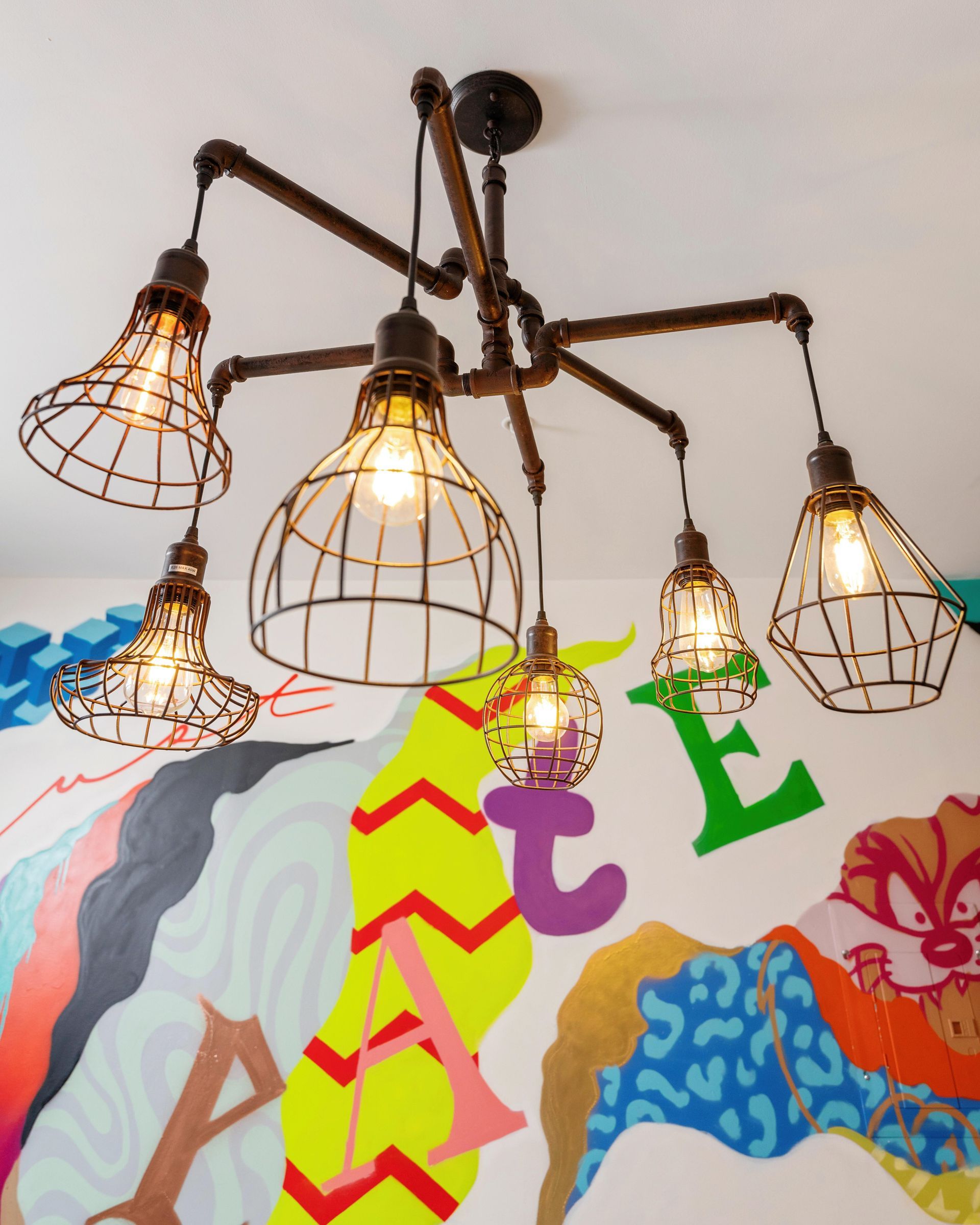 Cluster of five cage pendant lights glowing above a colorful painted wall mural