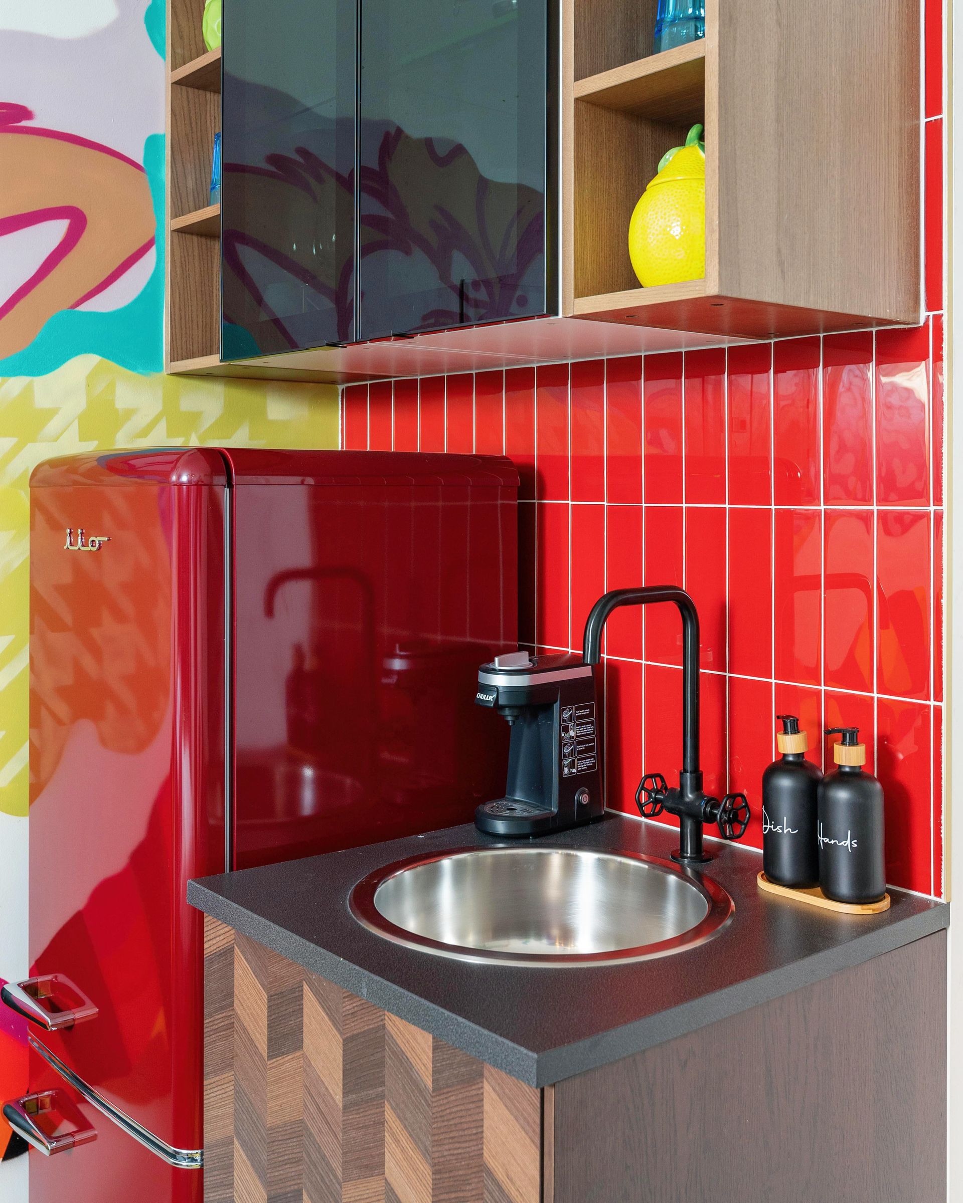 Compact kitchen corner with red tile backsplash, black sink, red fridge, and wooden cabinets