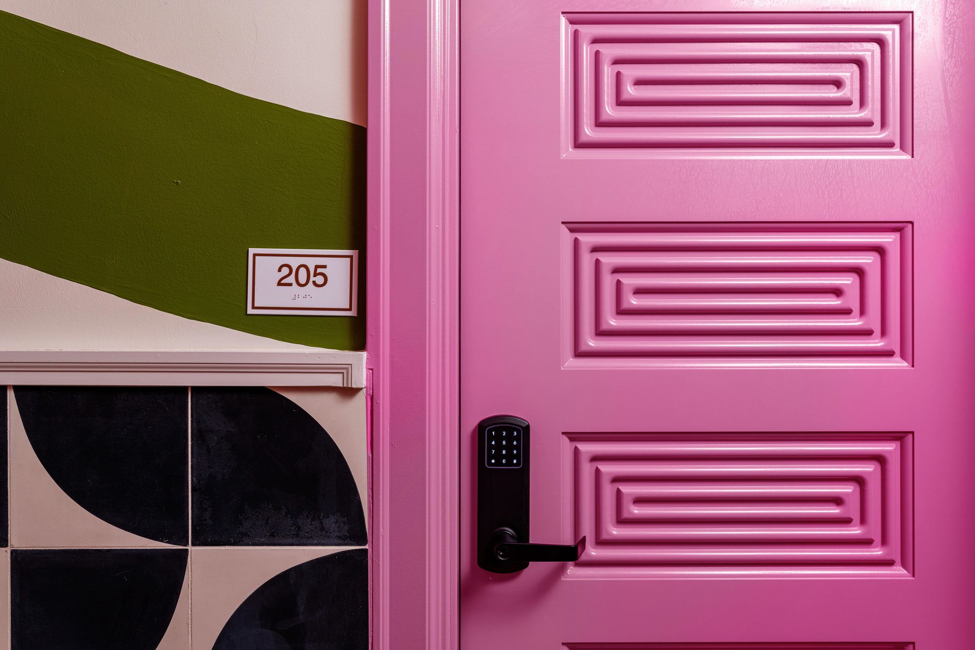 Pink front door with black handle and house number 206 beside a green-and-white wall.