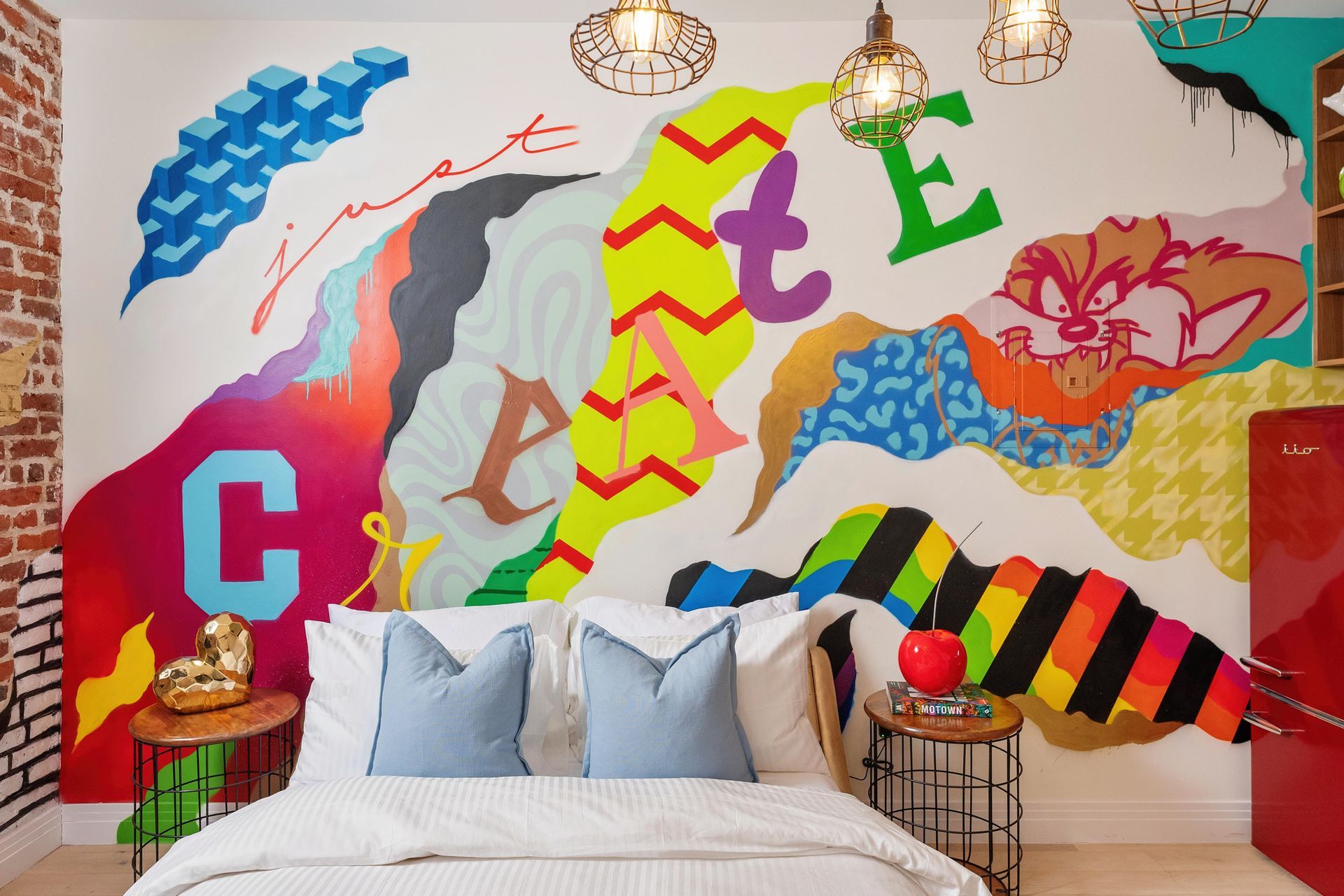 Colorful mural behind a bed with pillows, featuring bold letters, hearts, and abstract shapes