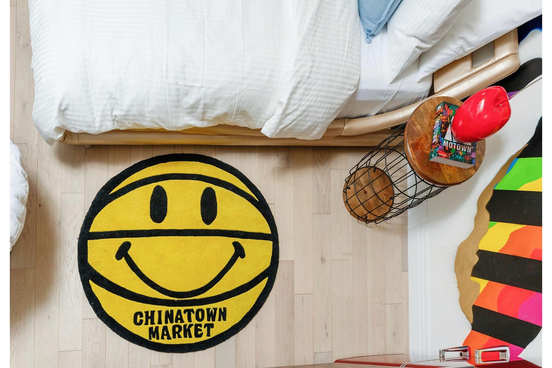 Yellow smiley-face rug on a light wood floor beside a bed and colorful striped decor.