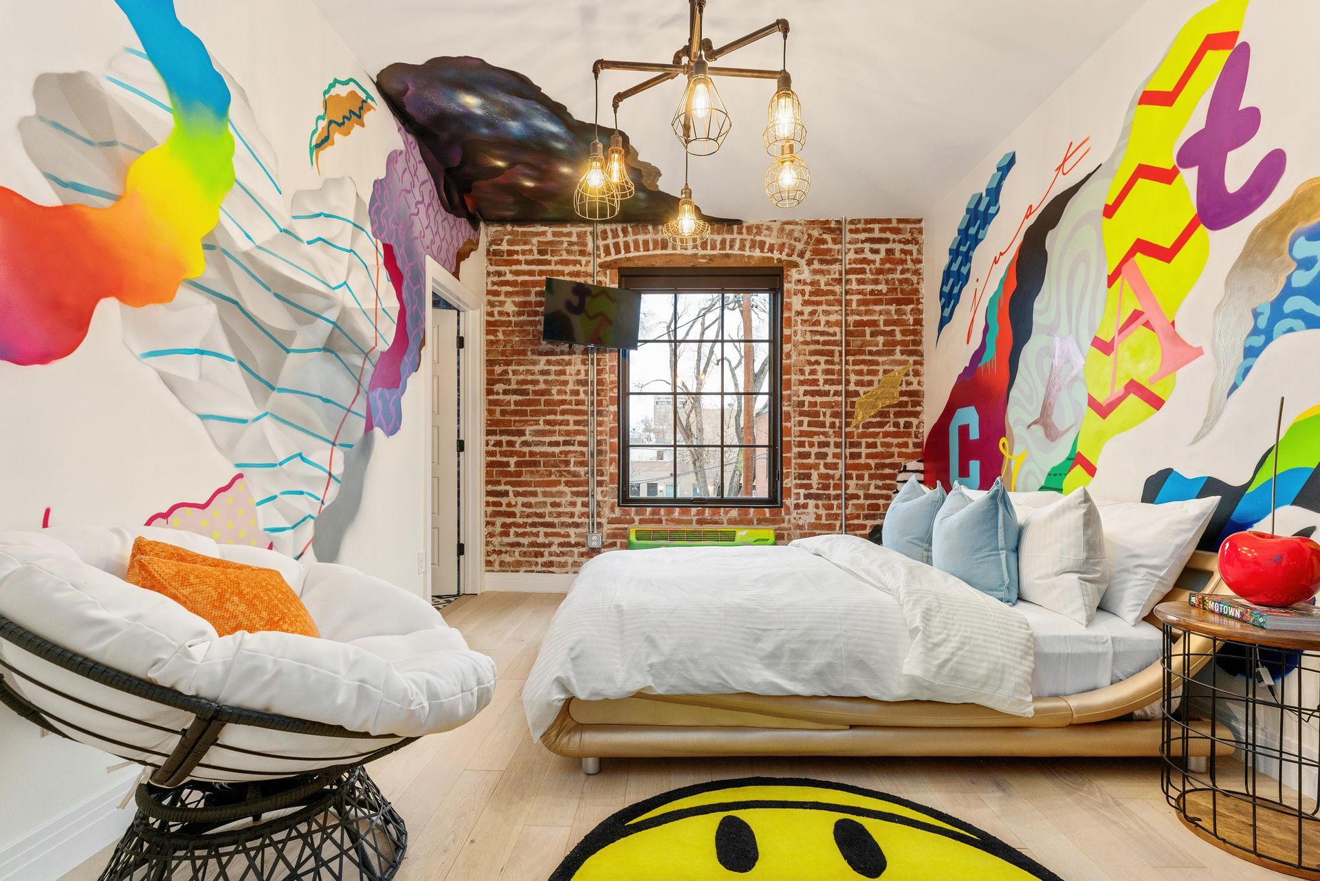 Bright colorful bedroom with graffiti-style wall art, brick fireplace, and white bedding