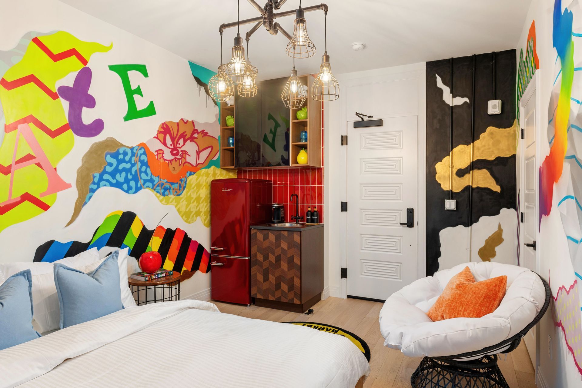Colorful bedroom with graffiti mural walls, twin beds, chandelier, and bright accent furniture