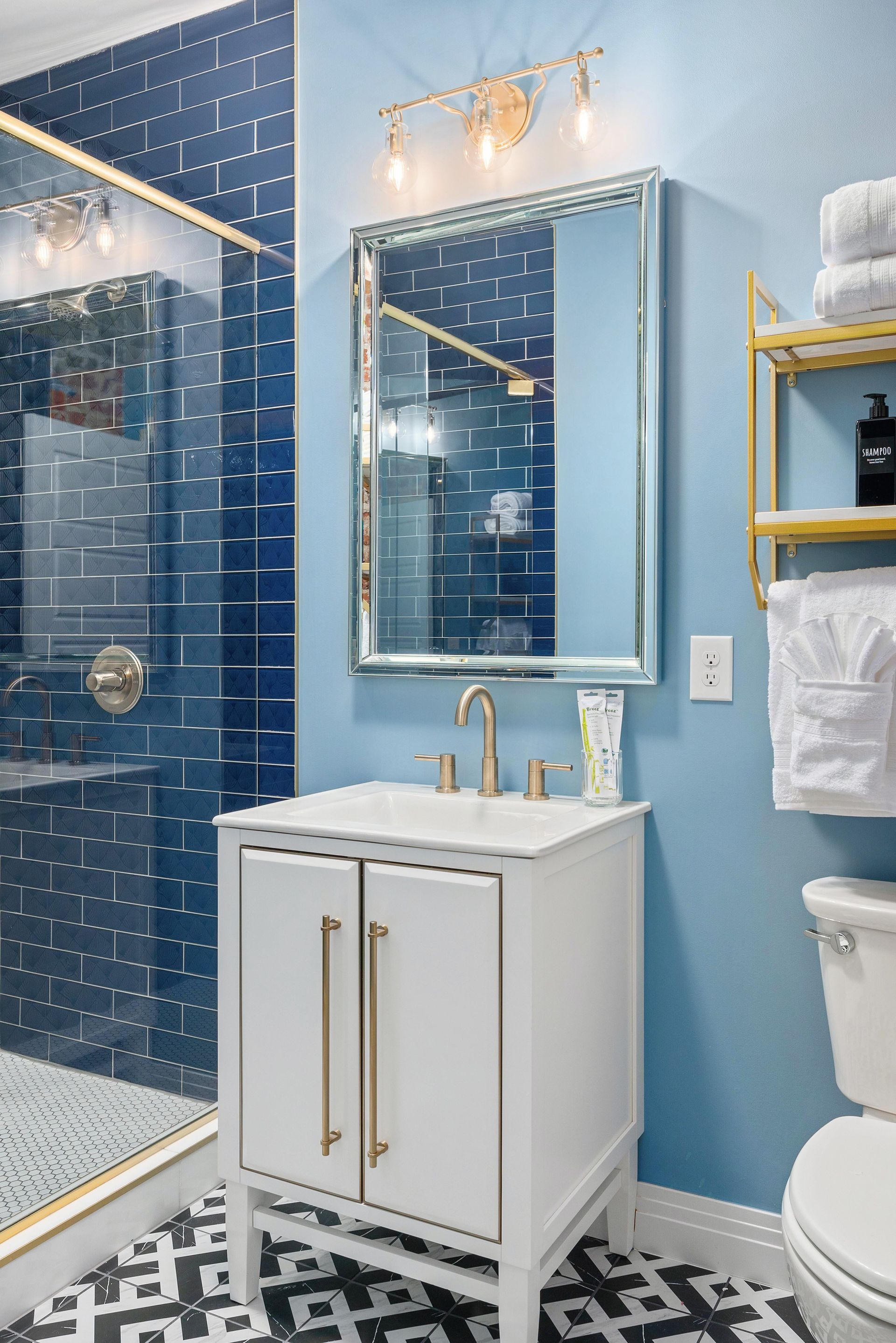 Bright blue bathroom with glass shower, gold fixtures, and a white vanity with mirror