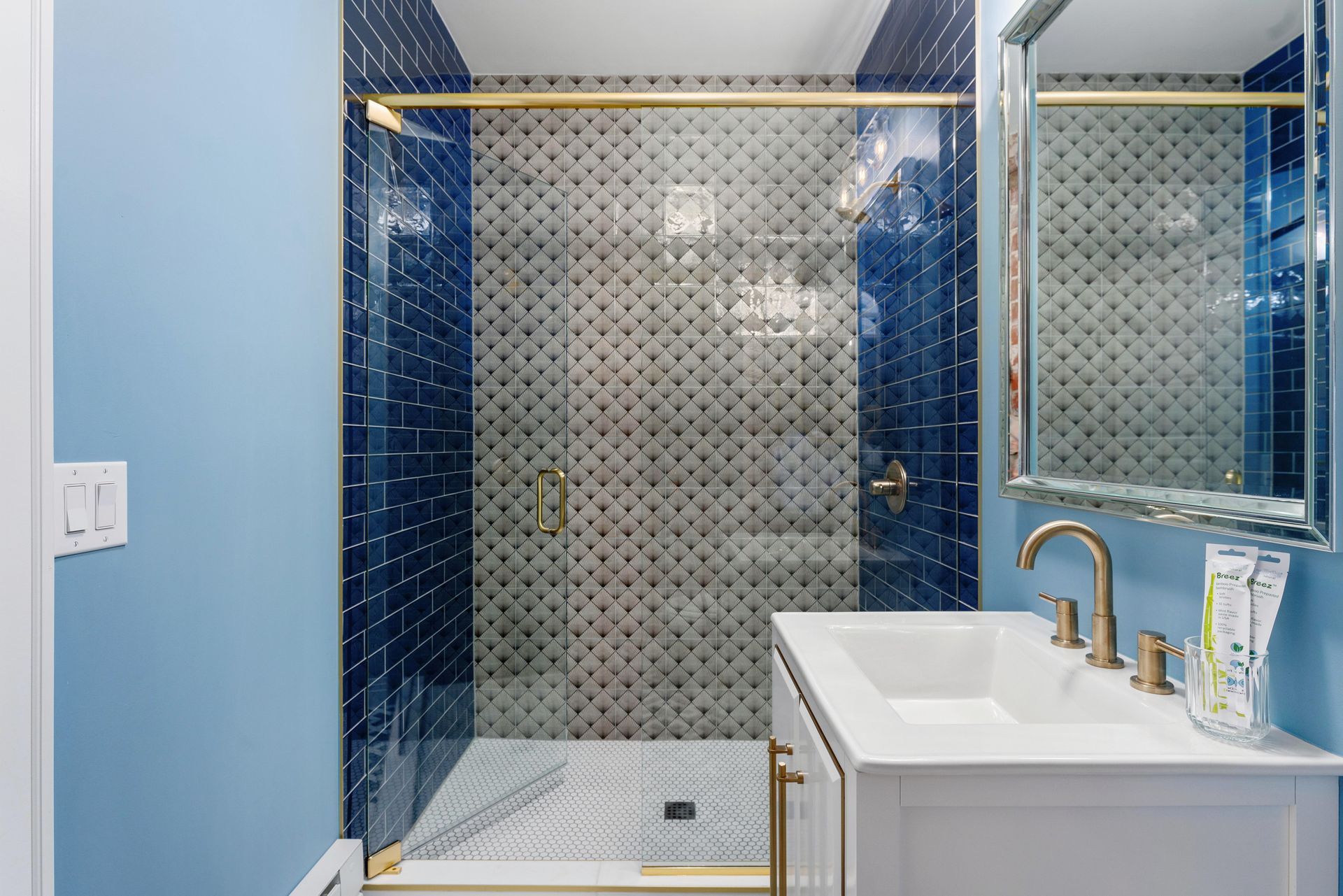 Modern bathroom with blue tiled shower, brass fixtures, and white vanity sink with mirror
