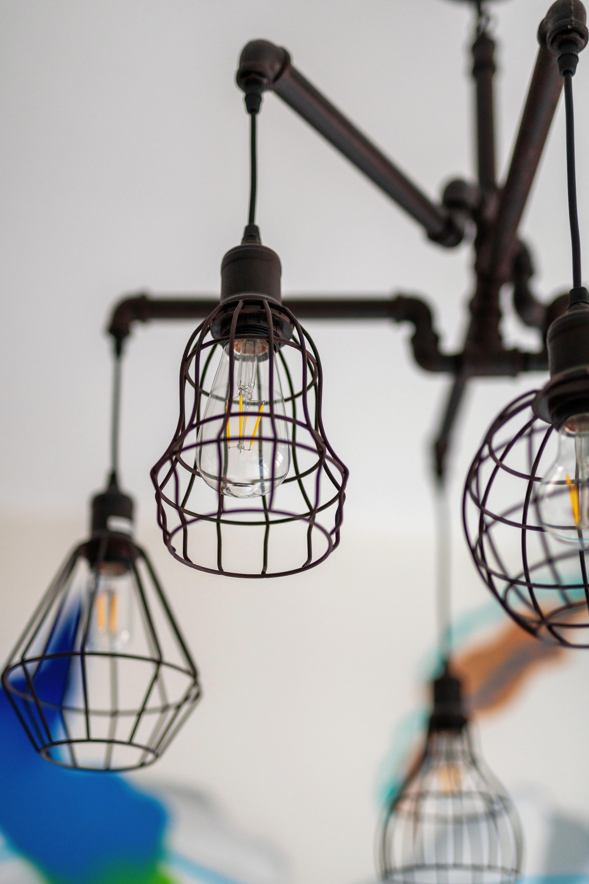 Metal cage pendant lights hanging from black arms against a blurred indoor background