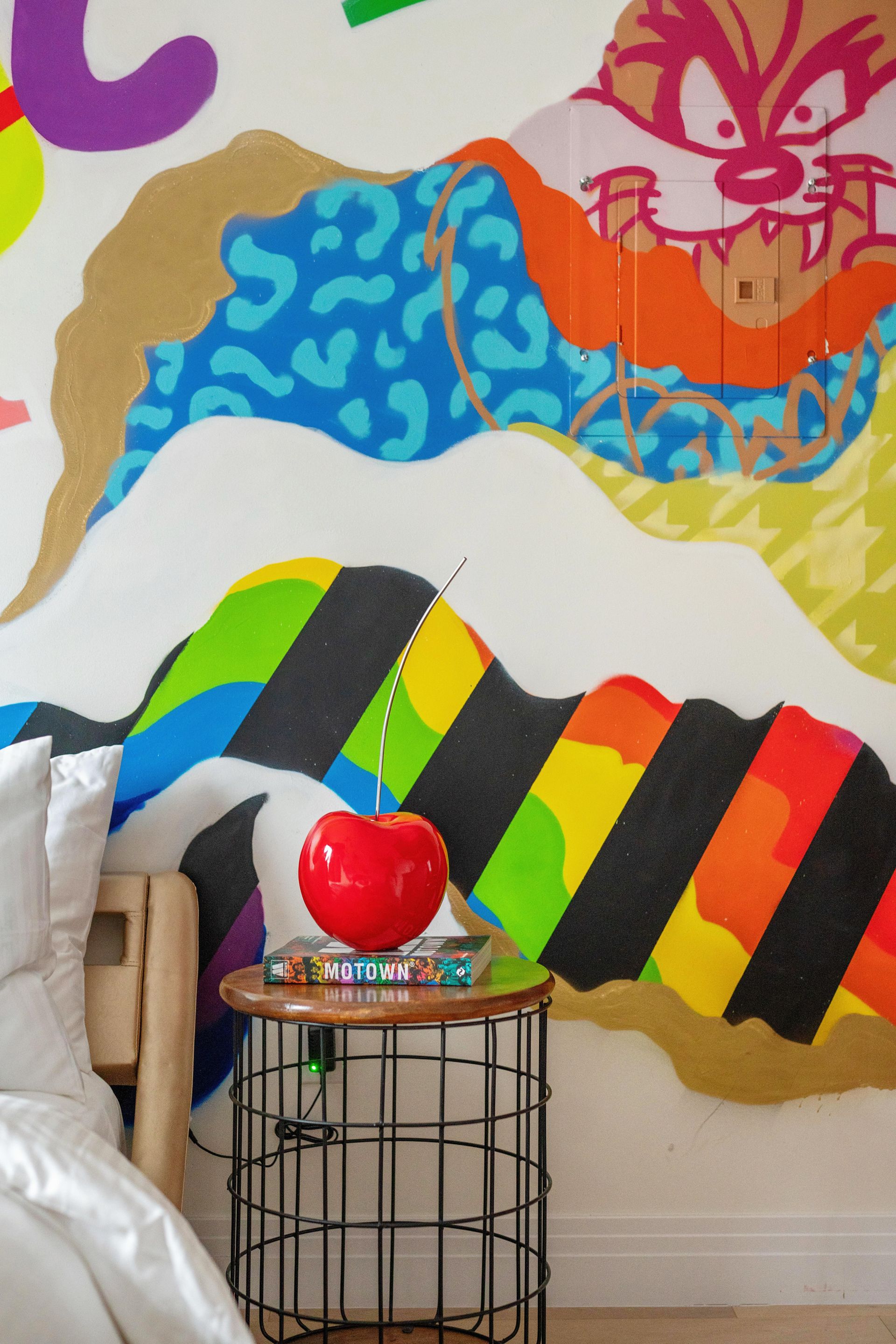 Colorful wall mural above a small table with a red apple and a woven basket chair